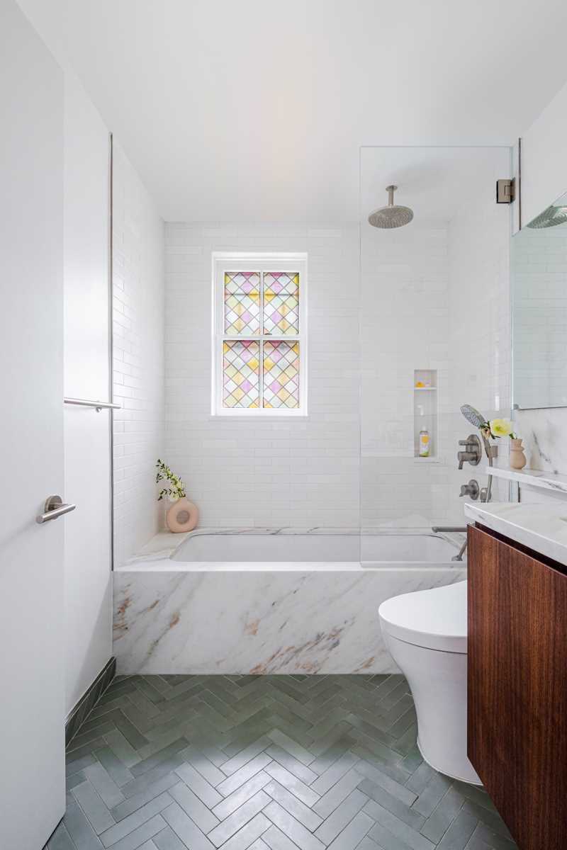 In this bathroom,  a stained glass window surrounded by white subway tiles creates a colorful accent.