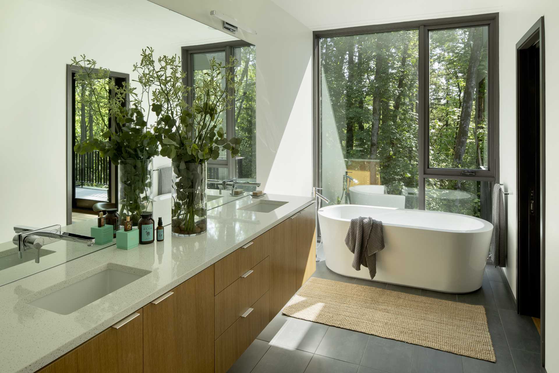 In this modern ensuite bathroom, a freestanding bathtub is positioned in front of the floor-to-ceiling window, while a double vanity is located below a large mirror.