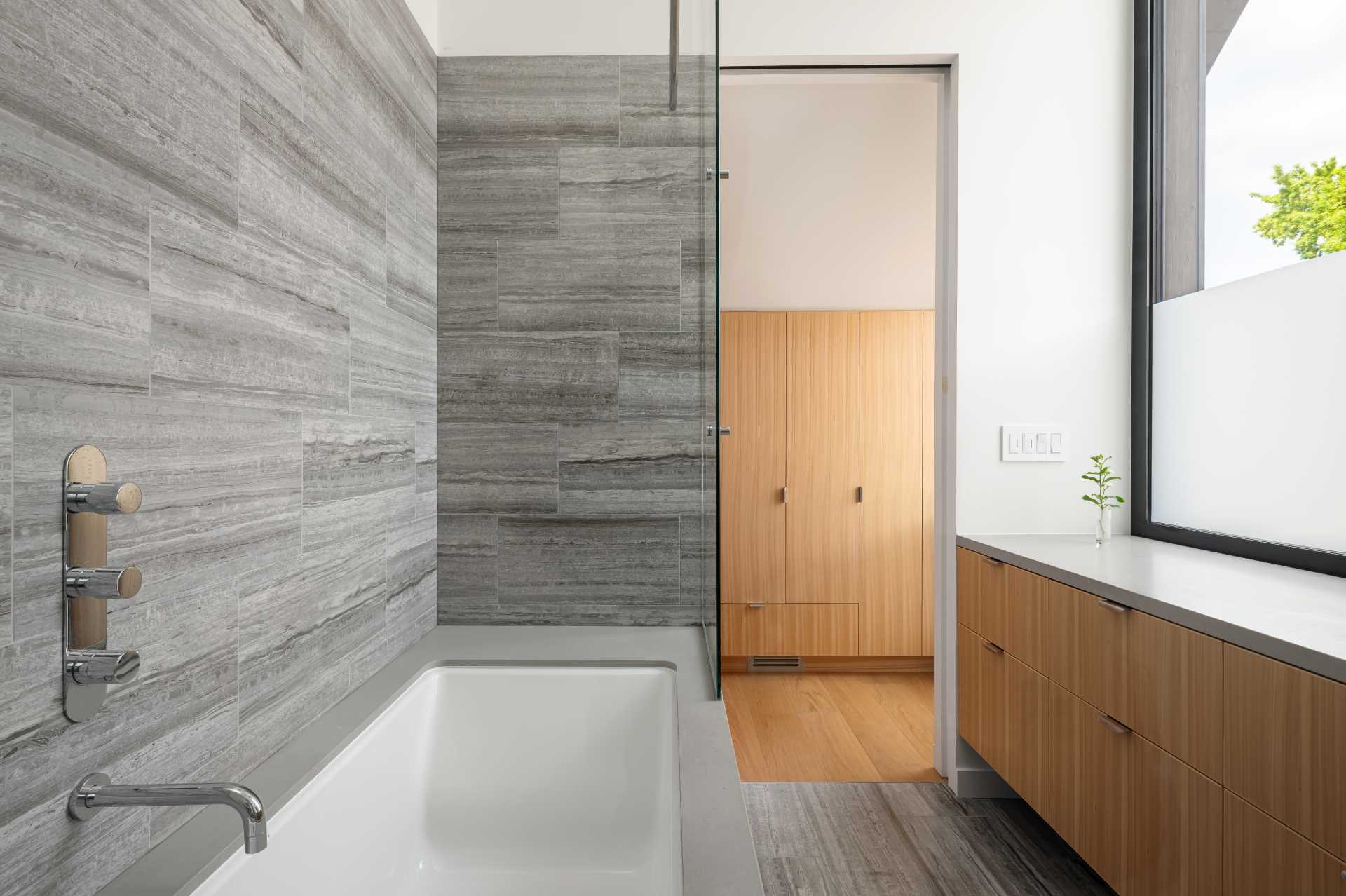 A modern bathroom with a high ceiling and window that matches the angle of the roof, as well as a built-in bathtub and a walk-in closet. 