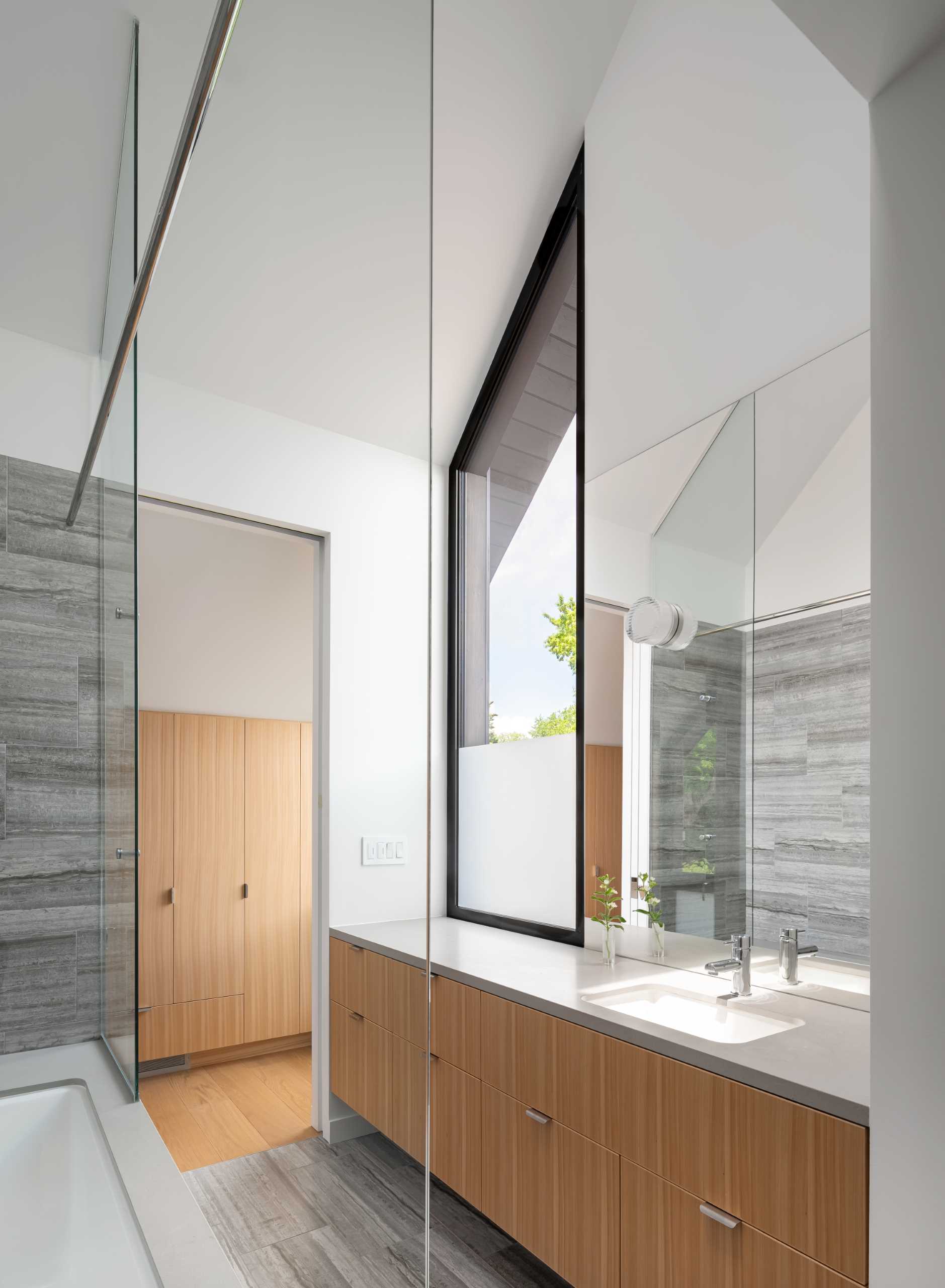 A modern bathroom with a high ceiling and window that matches the angle of the roof, as well as a built-in bathtub and a walk-in closet. 