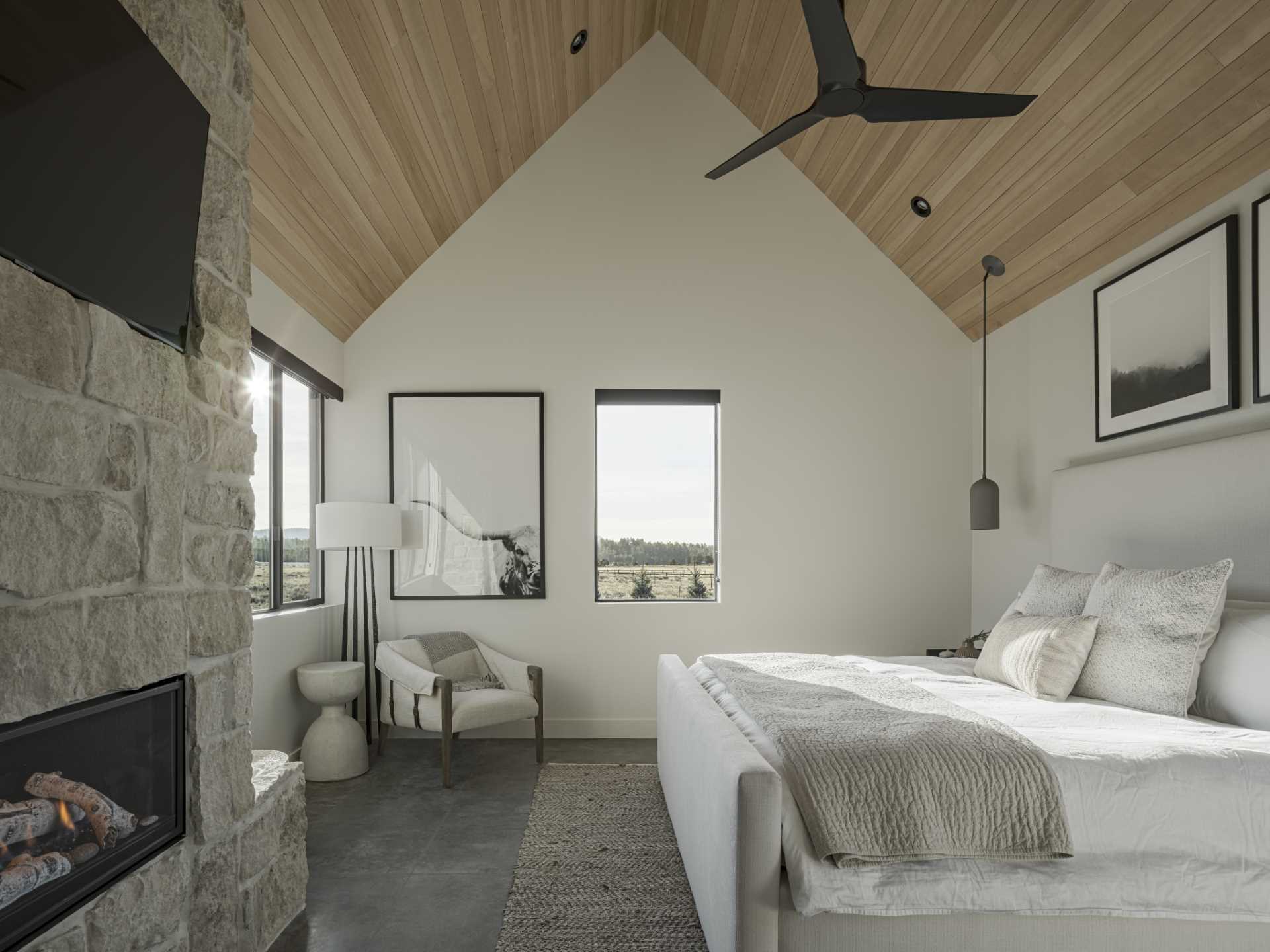 A modern bedroom with a stone wall, fireplace, and mountain views.