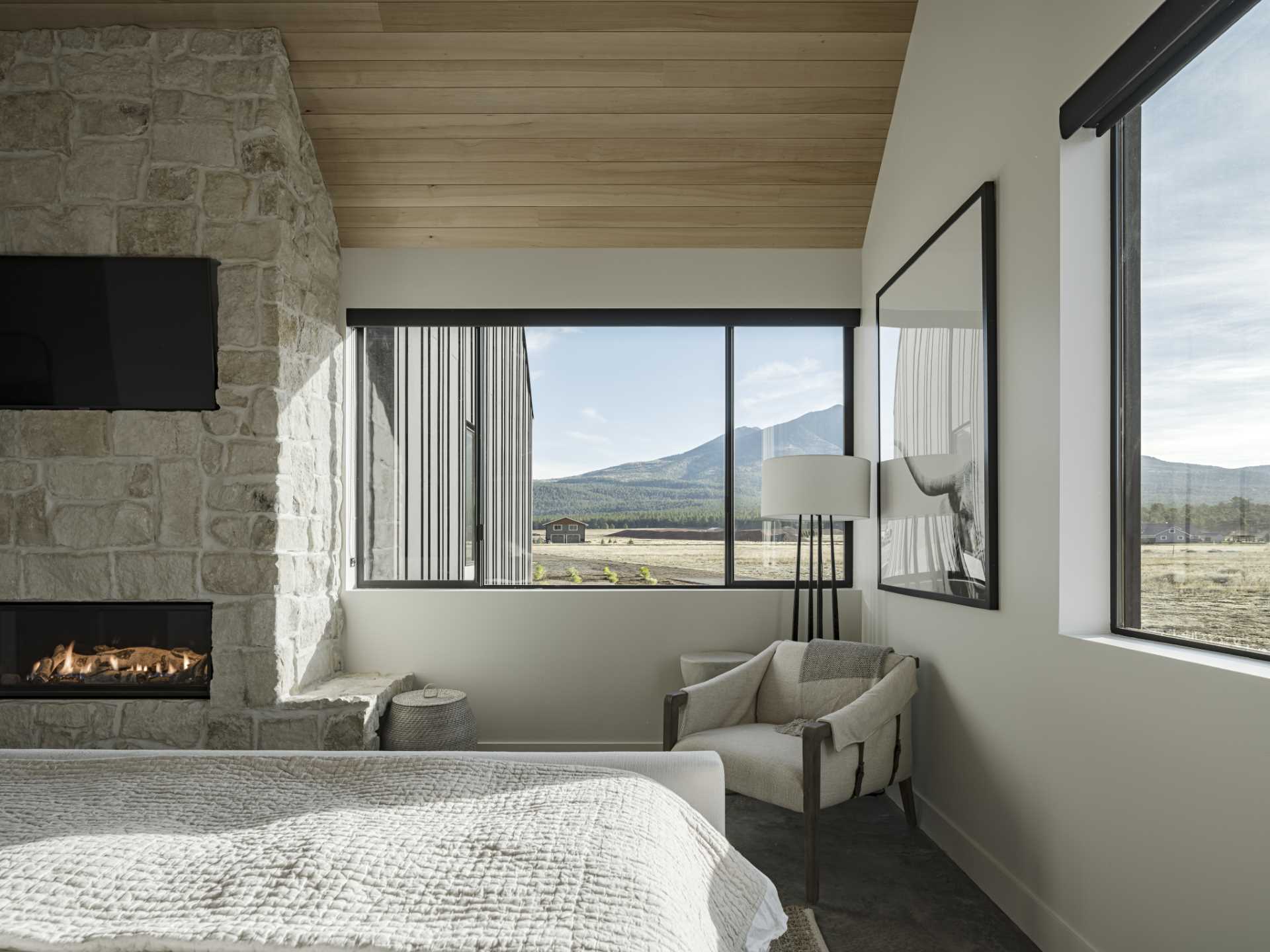 A modern bedroom with a stone wall, fireplace, and mountain views.