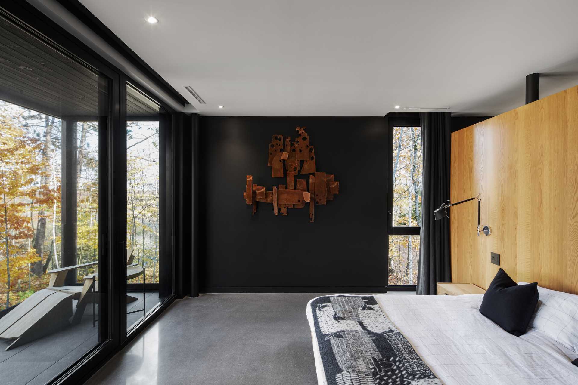 A modern bedroom with a wood accent wall adds warmth to the room, which has a concrete floor and opens to the deck.