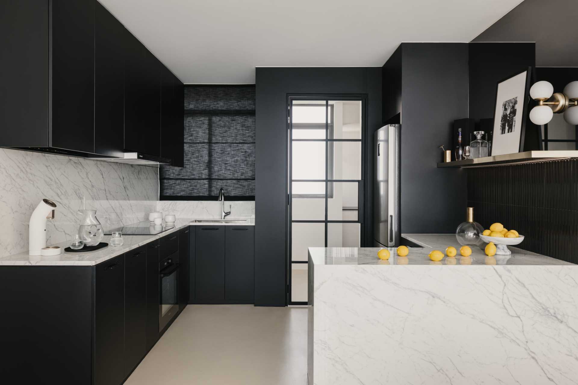 In this black and white kitchen, matte black cabinets and walls contrast the countertops and backsplash. Tiles and a blind add a textural element, while a mirrored area of the wall adds a touch of elegance and makes the ،e feel larger.