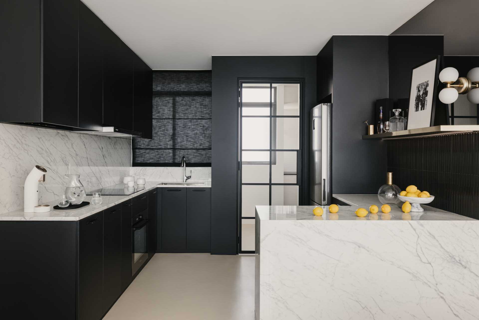 In this black and white kitchen, matte black cabinets and walls contrast the countertops and backsplash. Tiles and a blind add a textural element, while a mirrored area of the wall adds a touch of elegance and makes the space feel larger.