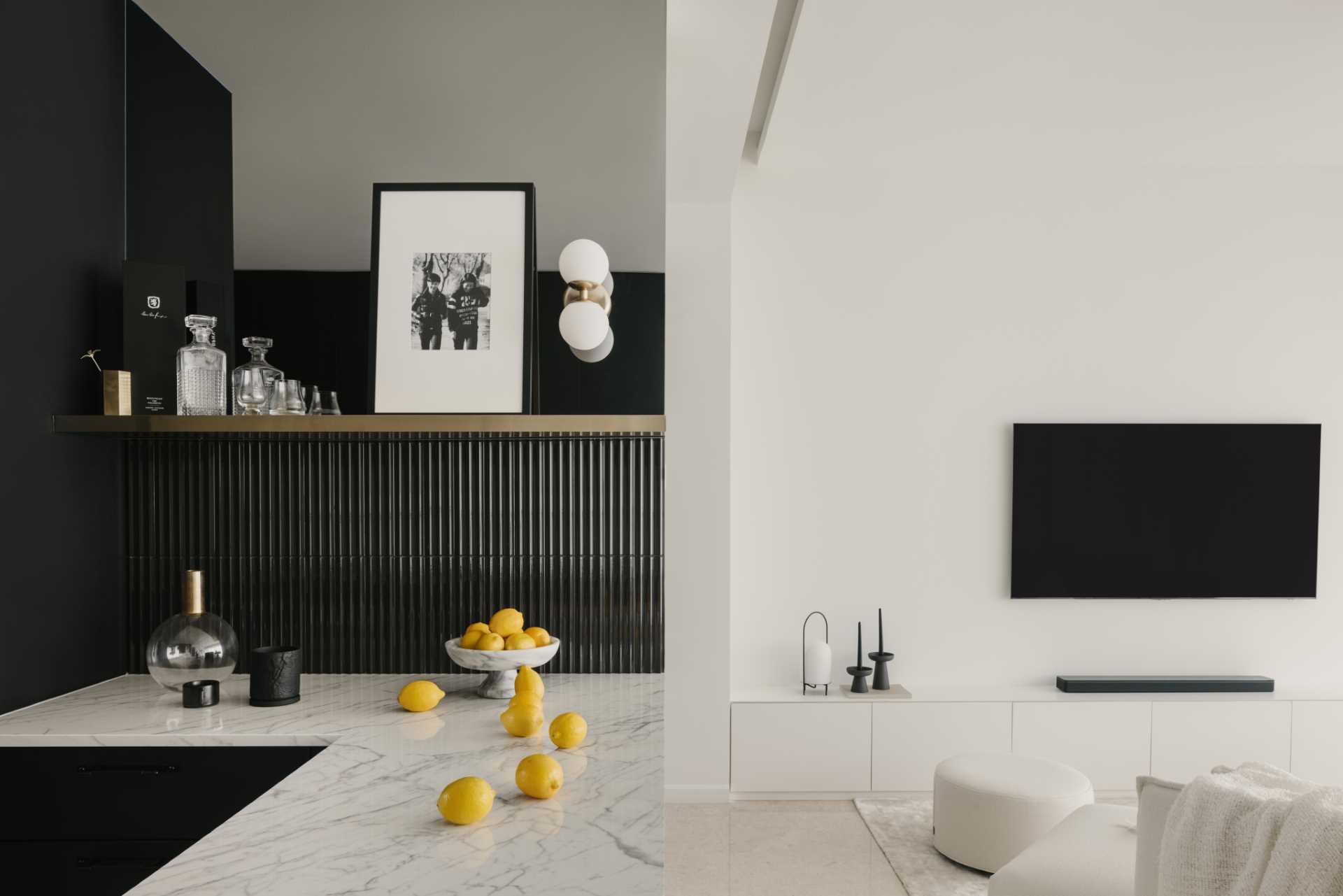 In this black and white kitchen, matte black cabinets and walls contrast the countertops and backsplash. Tiles and a blind add a textural element, while a mirrored area of the wall adds a touch of elegance and makes the space feel larger.