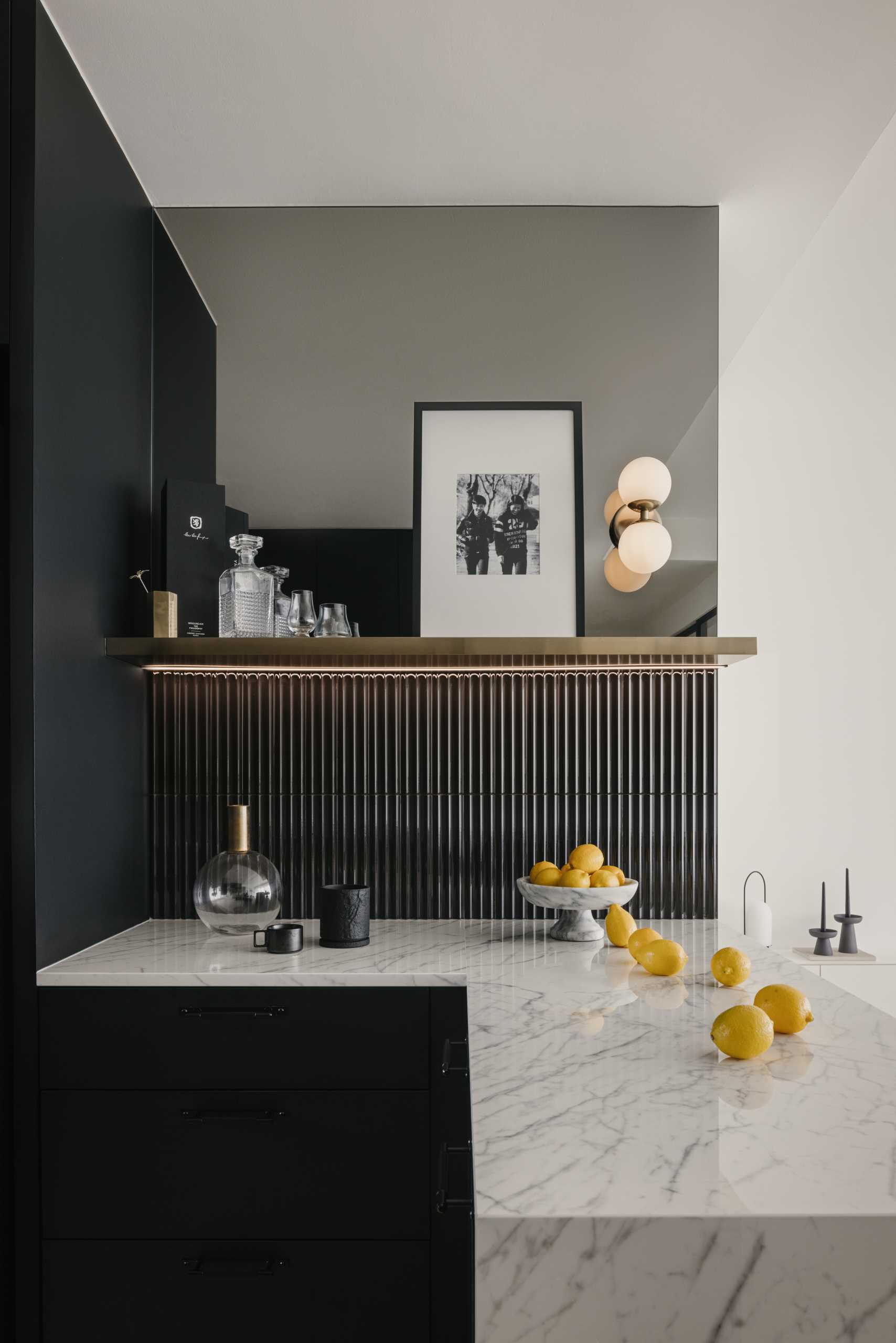 In this black and white kitchen, matte black cabinets and walls contrast the countertops and backsplash. Tiles and a blind add a textural element, while a mirrored area of the wall adds a touch of elegance and makes the space feel larger.