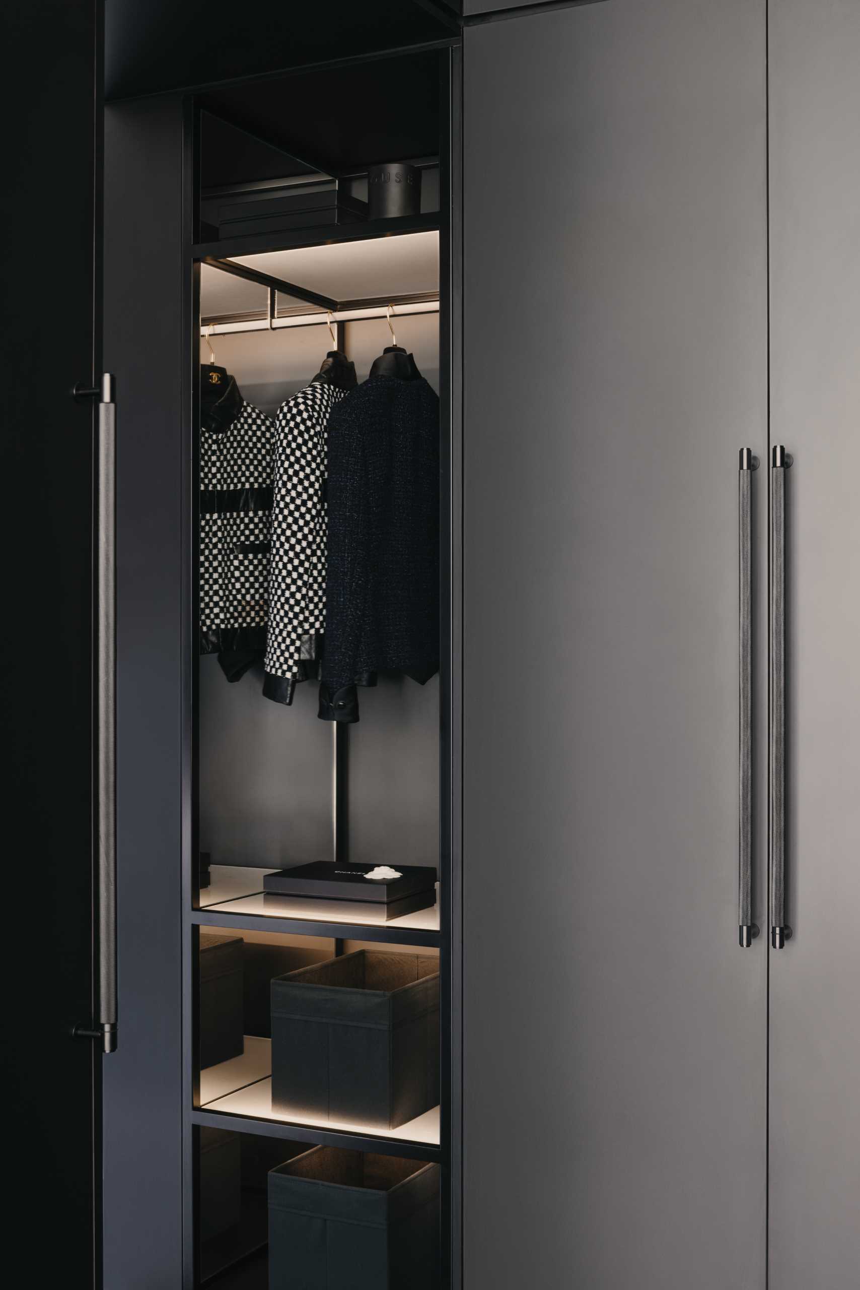 A white sliding door in a bedroom opens to reveal a walk-in closet and dressing room, where a pair of mirrors hang from the ceiling, and black closet cabinetry with hidden lighting creates a luxurious atmosphere.