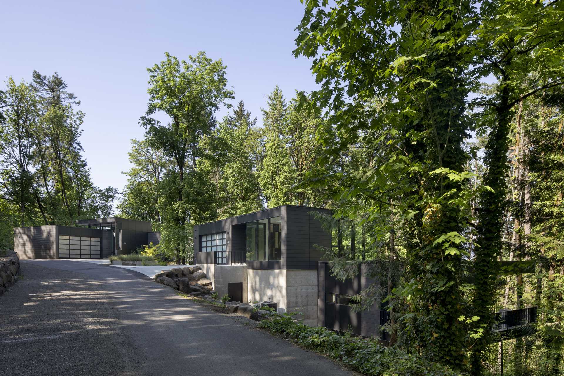 A modern black house on a steep site in the forest is spread out across multiple levels.