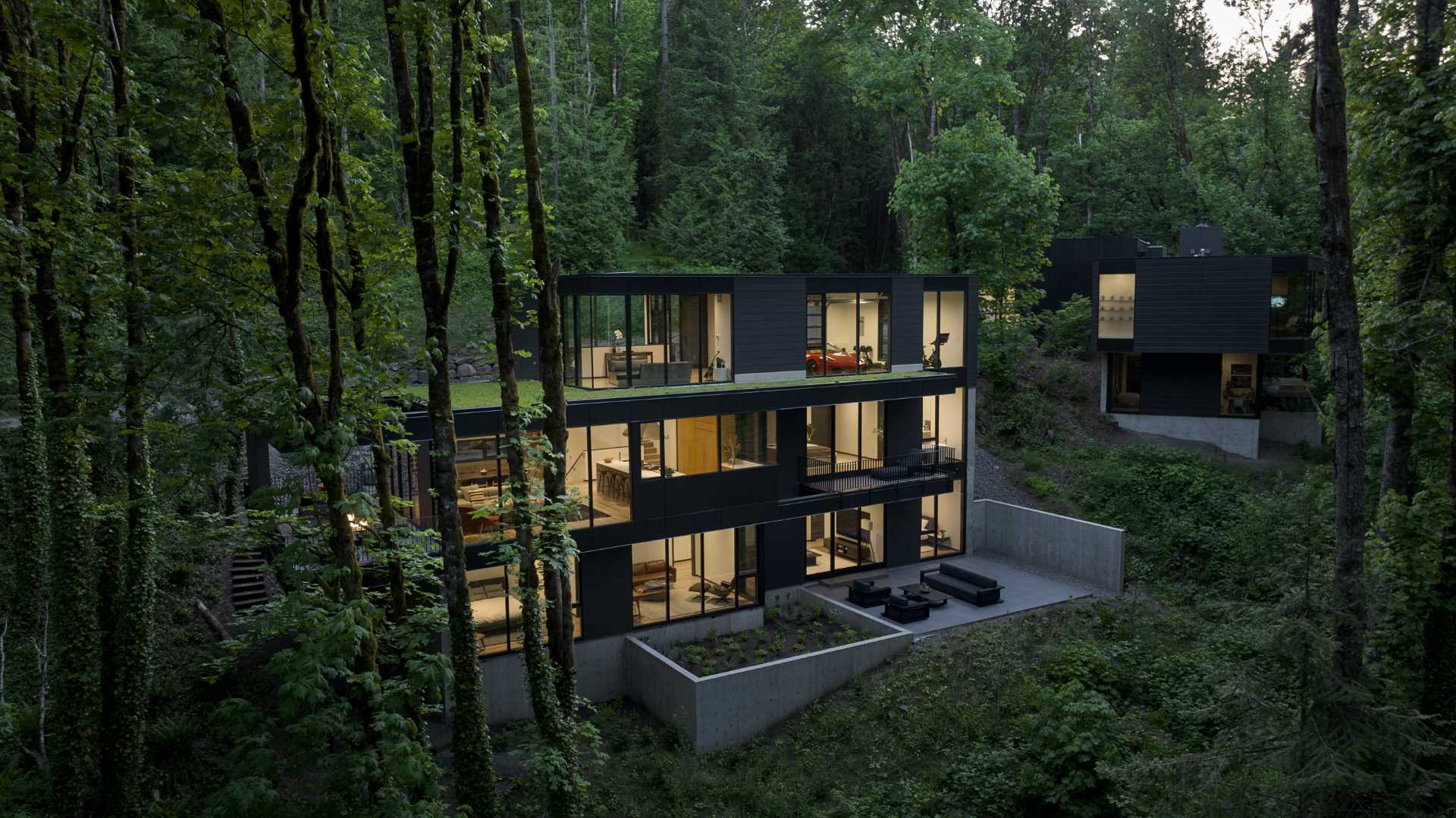 A modern black house in the forest is spread out across multiple levels.