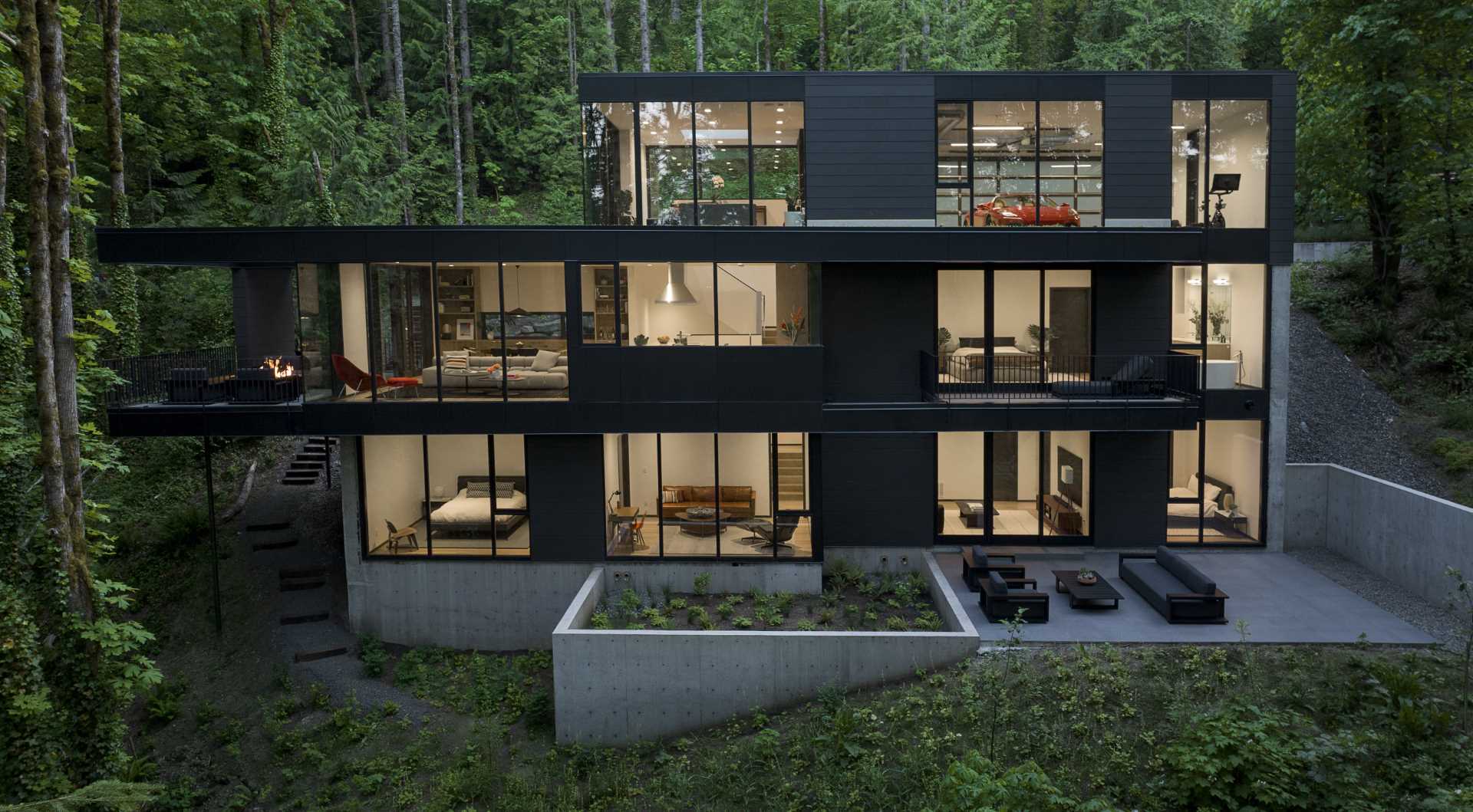 A modern black house in the forest is spread out across multiple levels.