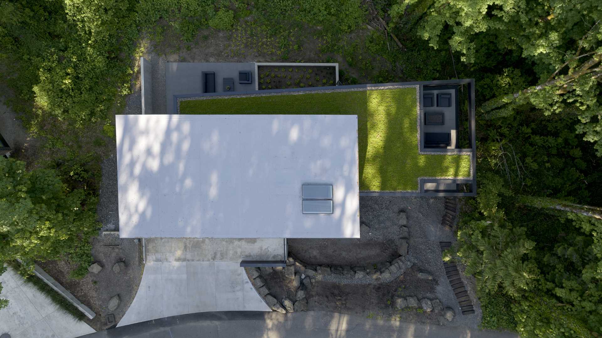 A modern black house in the forest has a green roof and is spread out across multiple levels.
