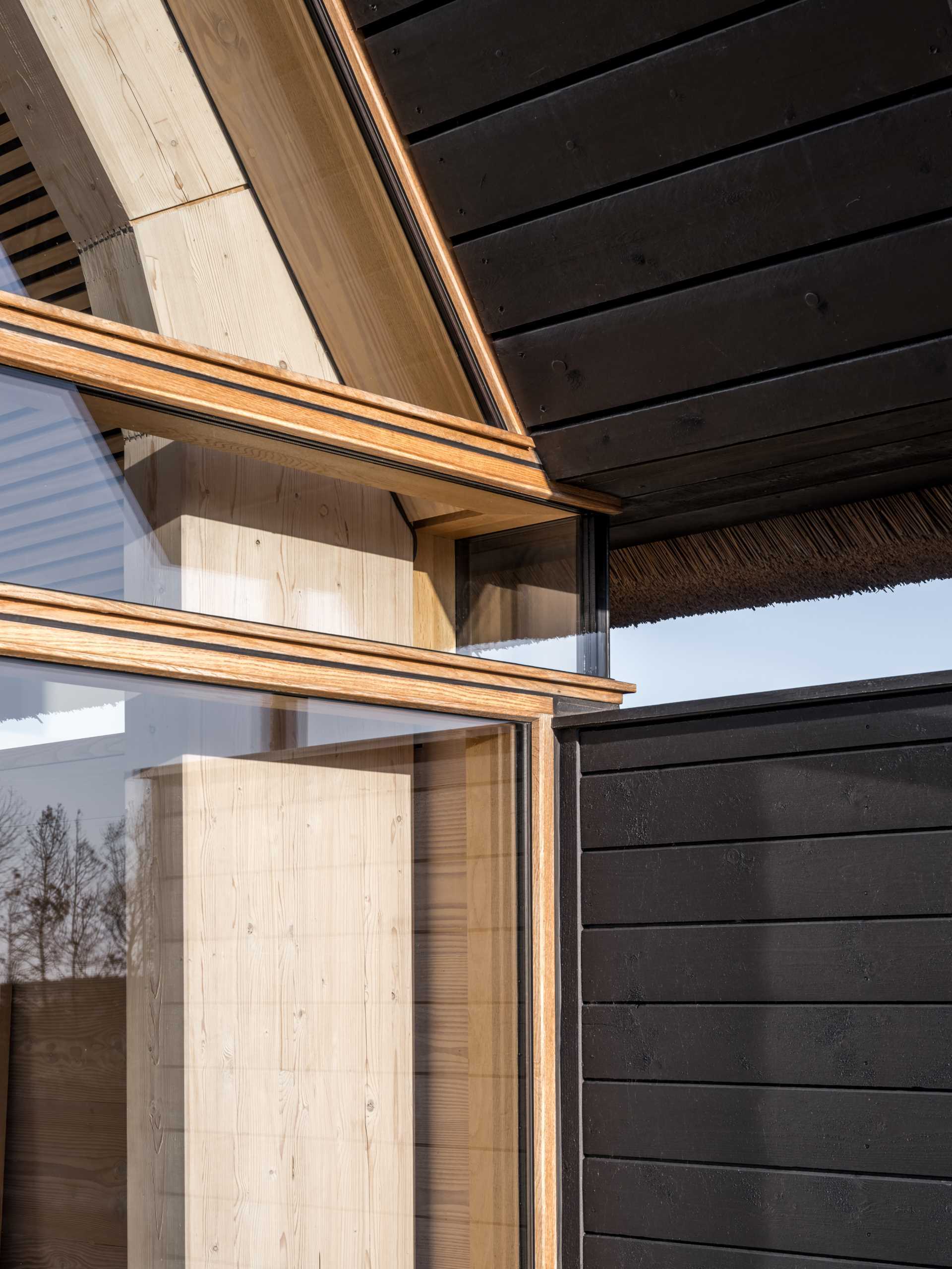 A modern home with a wall of windows, charred wood siding, and a thatched roof.