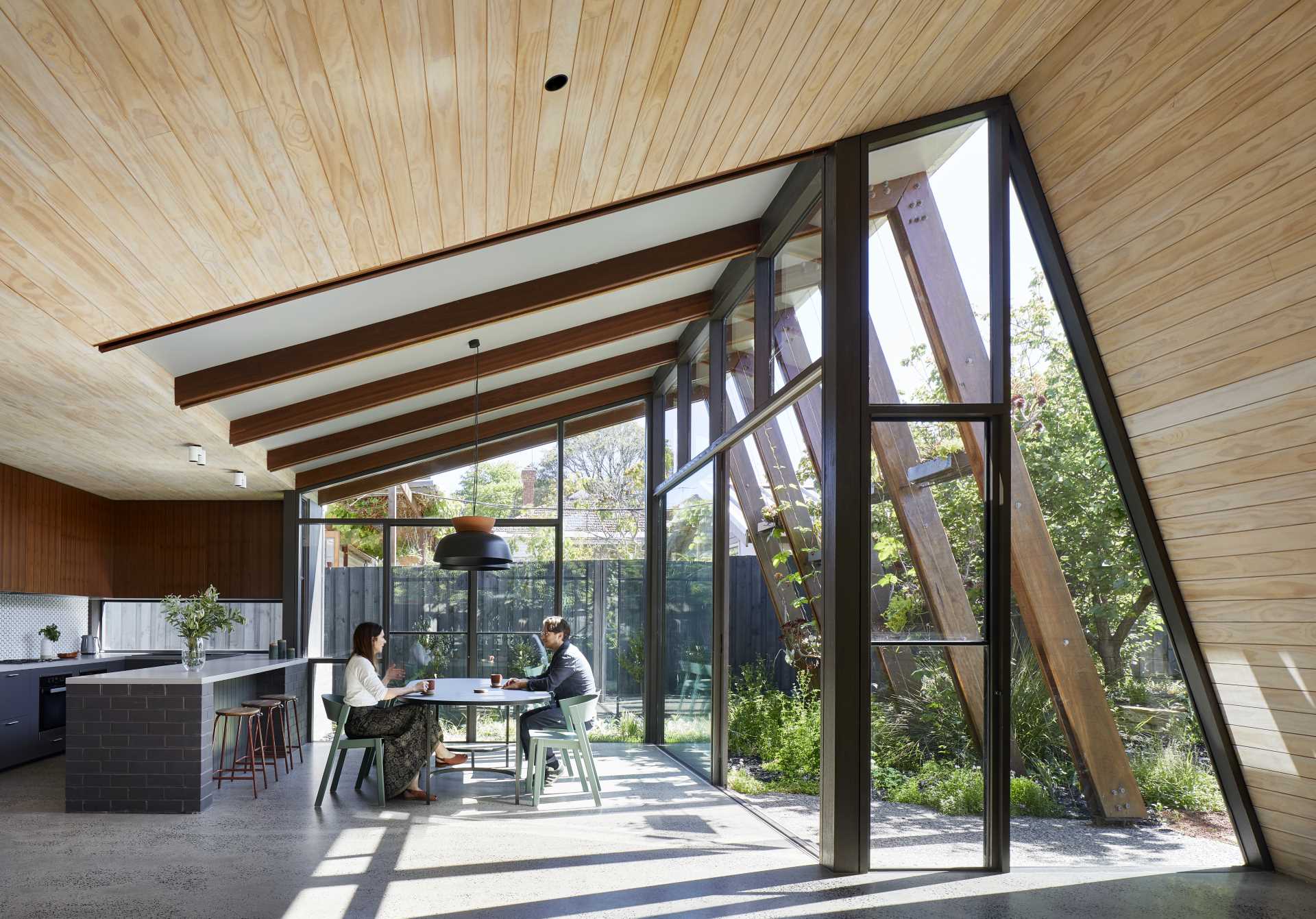 The arbor-like structure of this modern home addition includes shelving and wire guides that over time, will allow the plants to grow, providing shade and privacy for the interior.