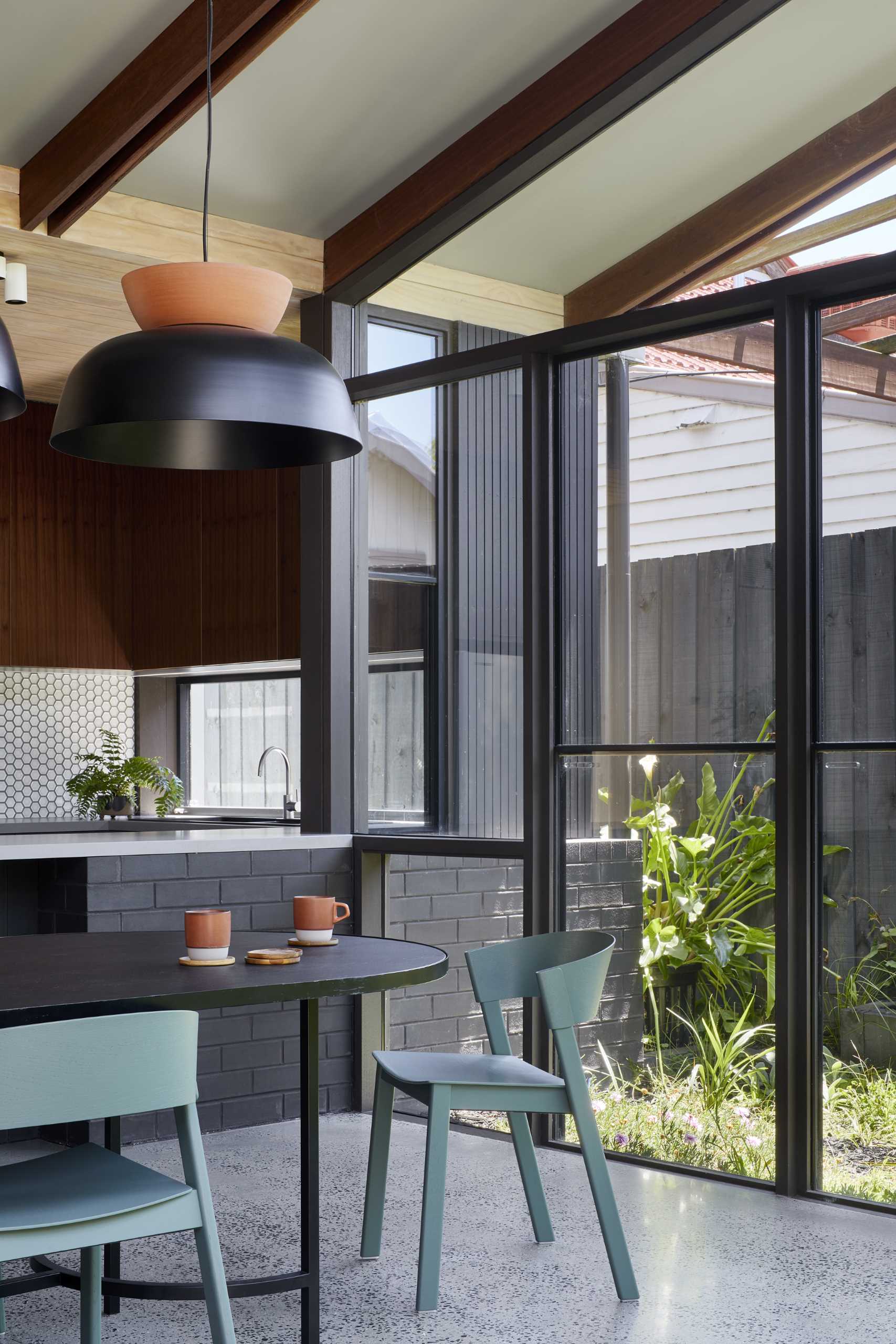 The dining area and kitchen are finished in greys, charcoals, and dusty greens, creating the perfect backdrop to offset and complement the garden's lush green.