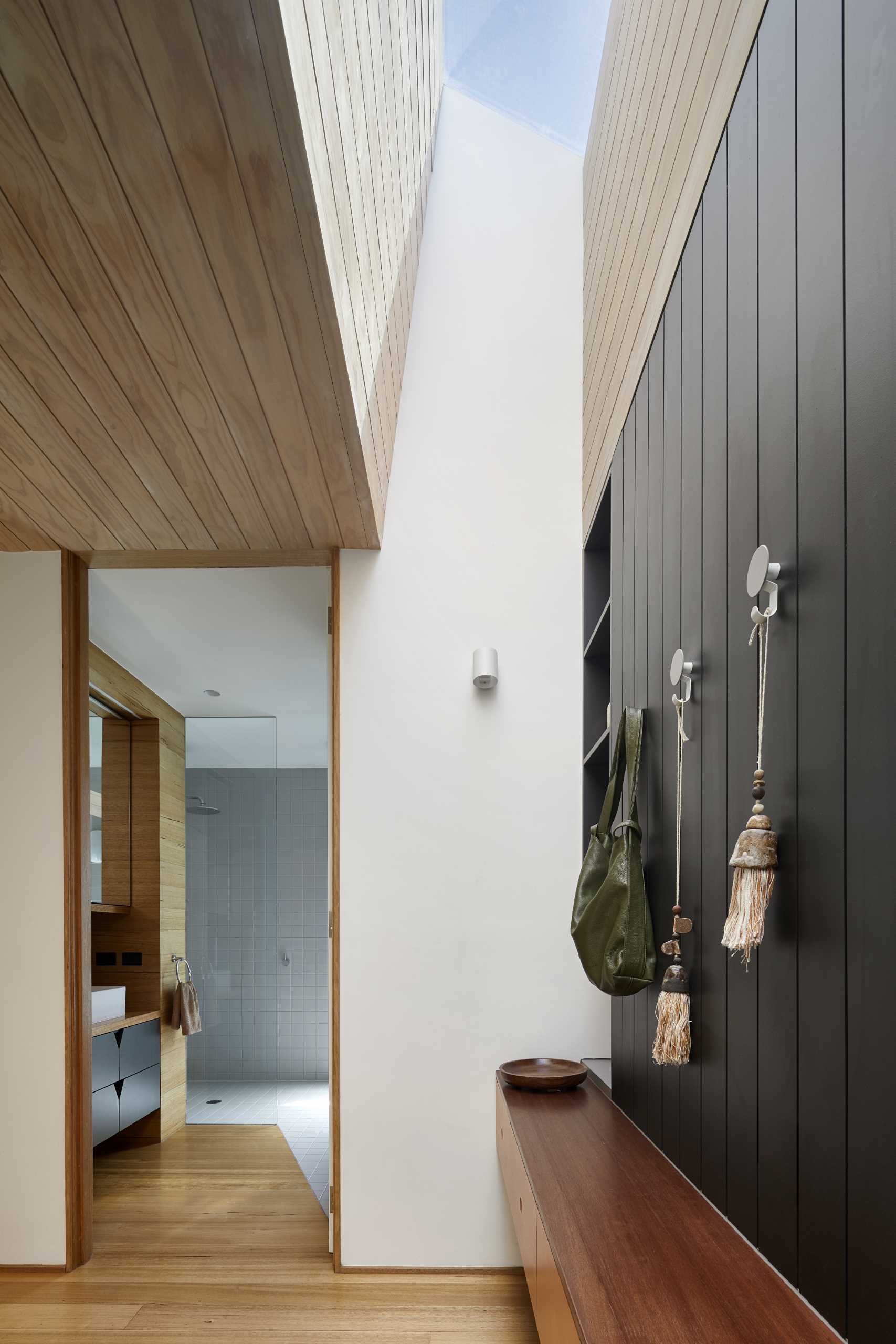 A modern bathroom includes a combination of wood flooring and square grey tiles that travel from the floor to the shower wall, while the vanity is built-in and includes dark grey cabinetry.