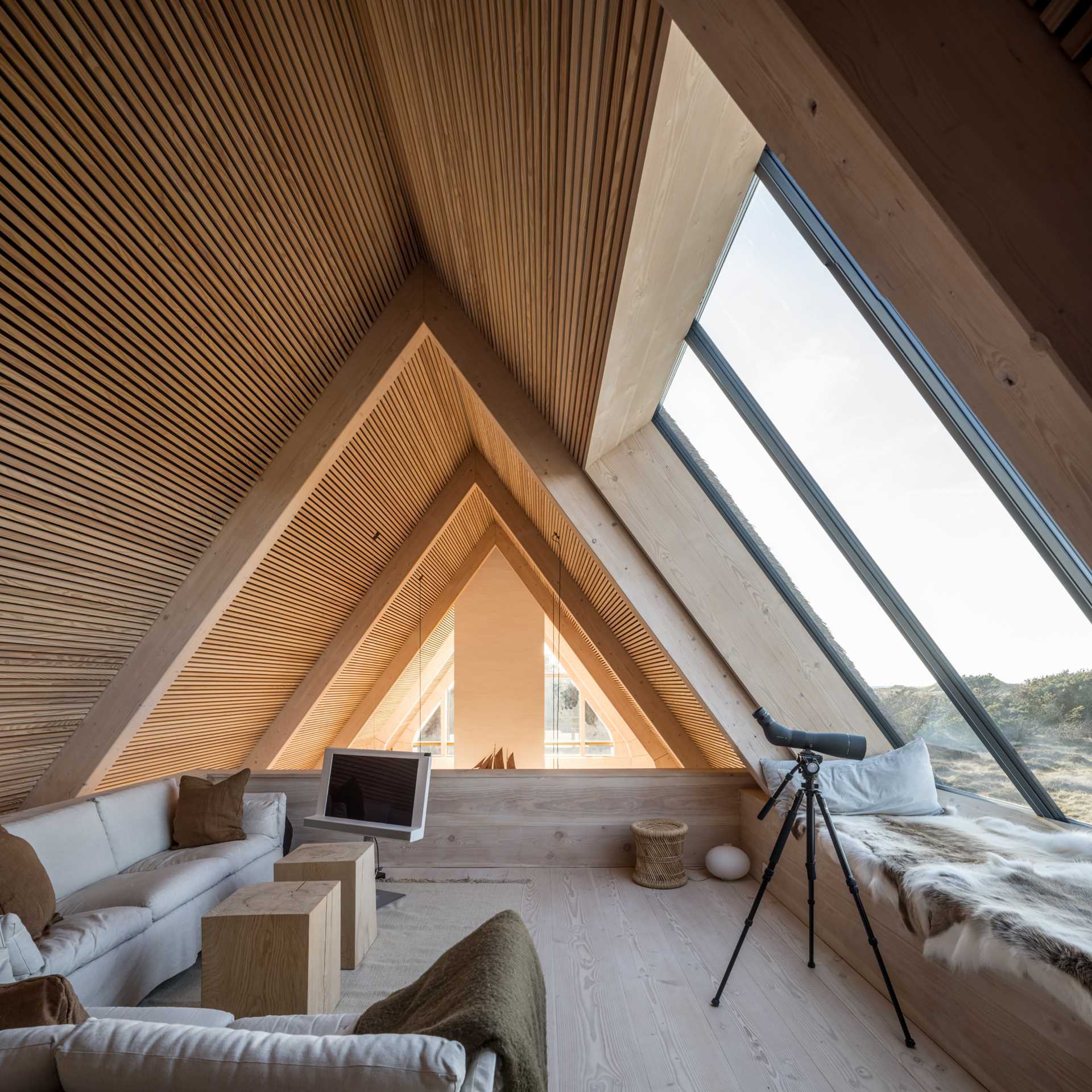 A modern house has a sitting area at the top of the home that's filled with natural light from the angled window.