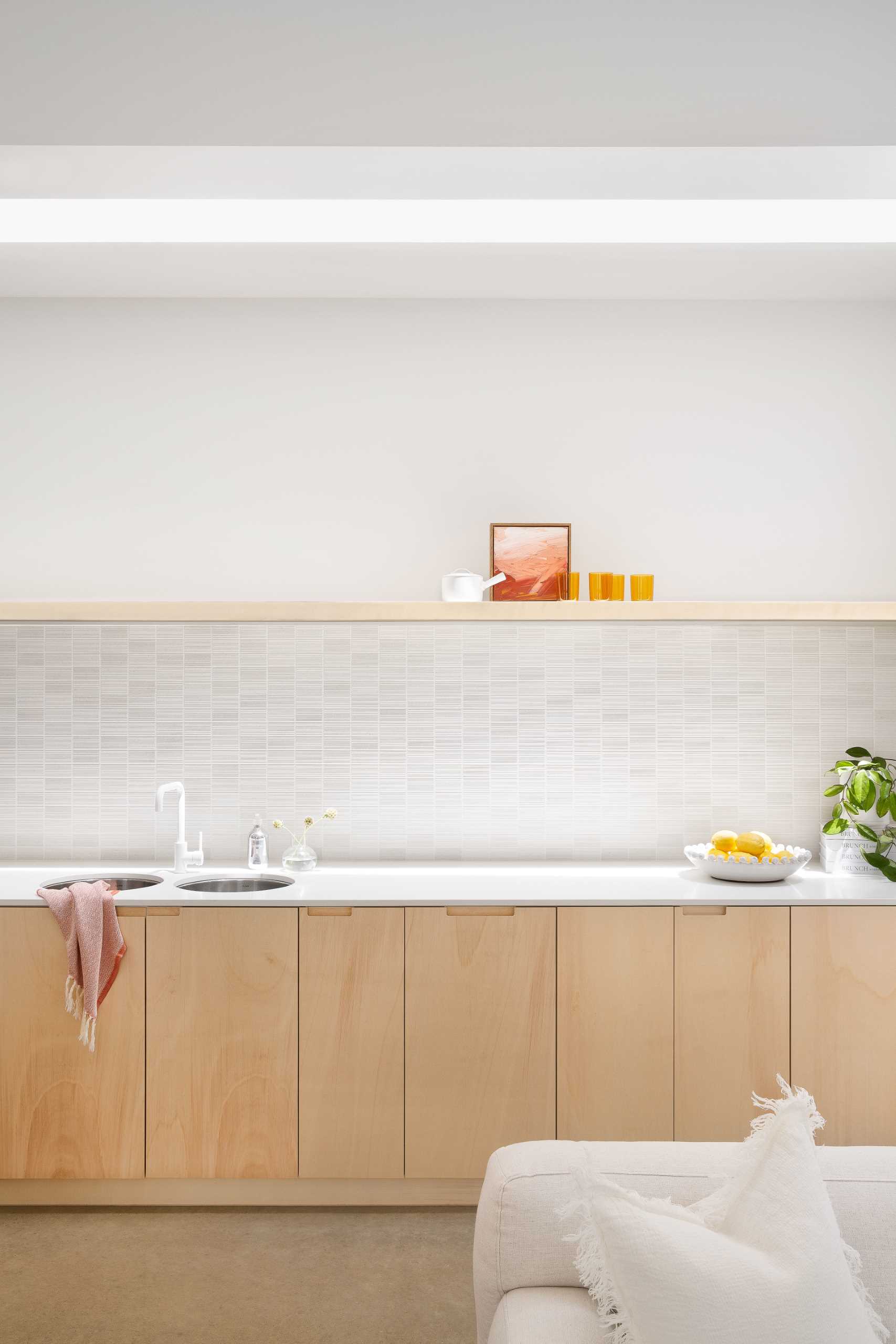 The kitchen, which enjoys natural light from a skylight above and has wood cabinets as well as a floating shelf, is located along the wall and behind the couch.