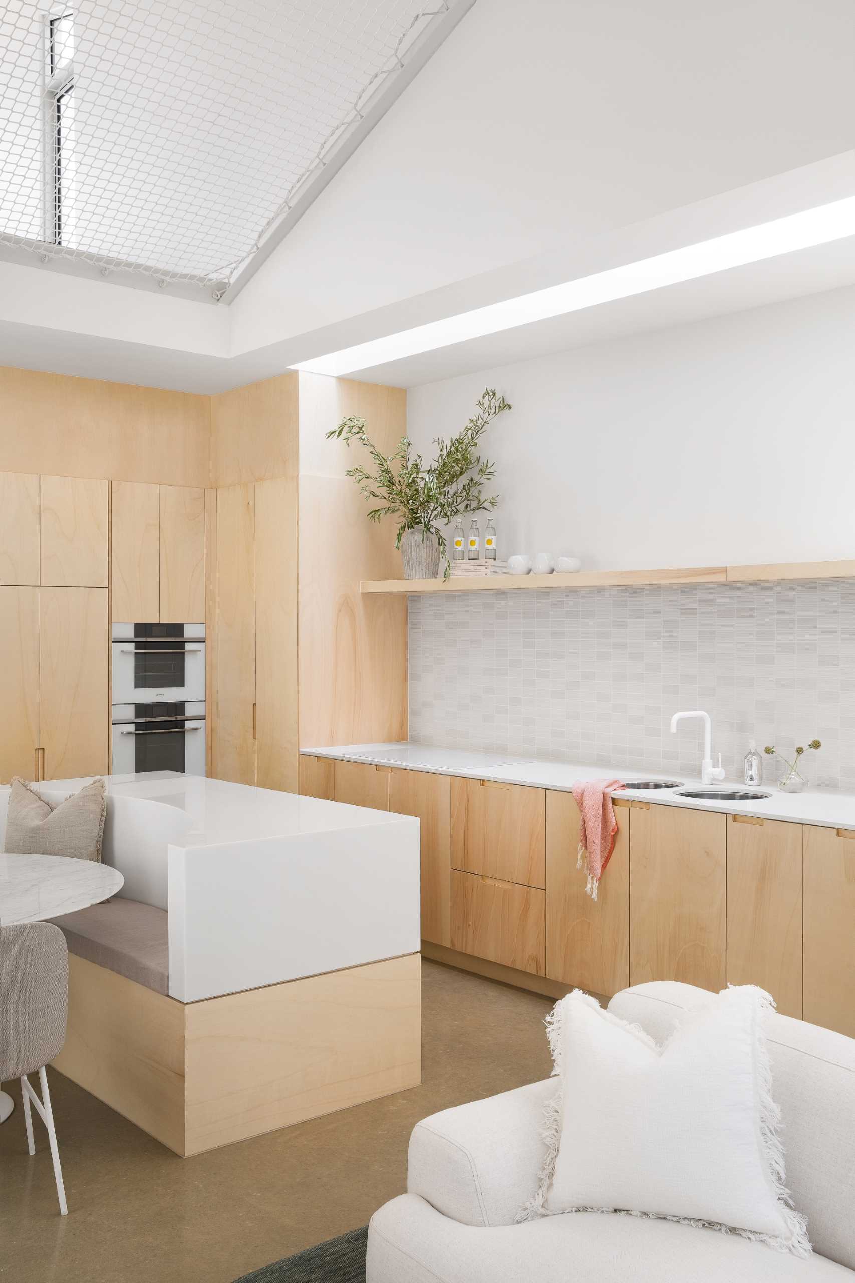 A modern wood and white kitchen with a floating shelf includes an island with built-in seating for the dining area.