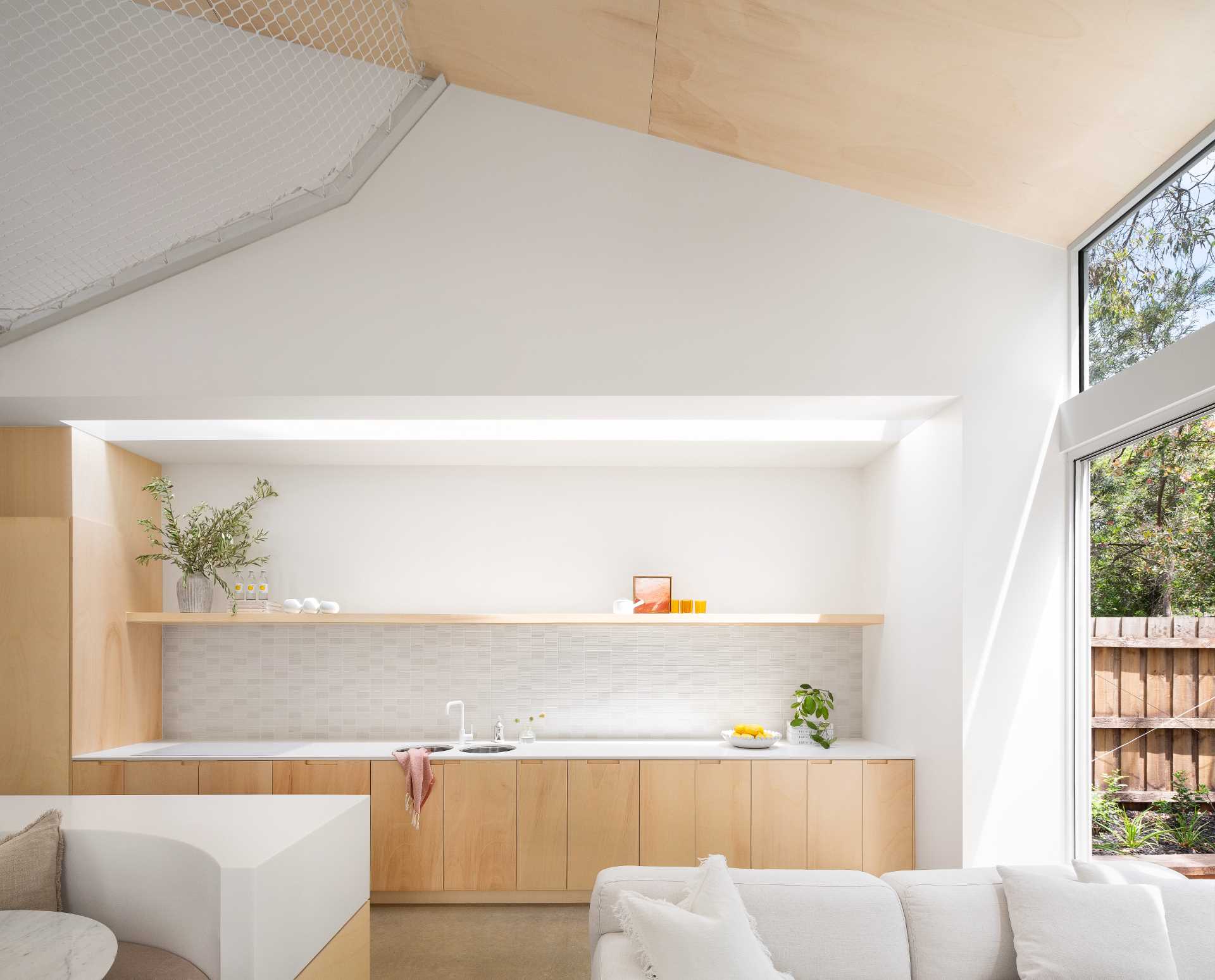 A modern wood and white kitchen with a floating shelf includes an island with built-in seating for the dining area.