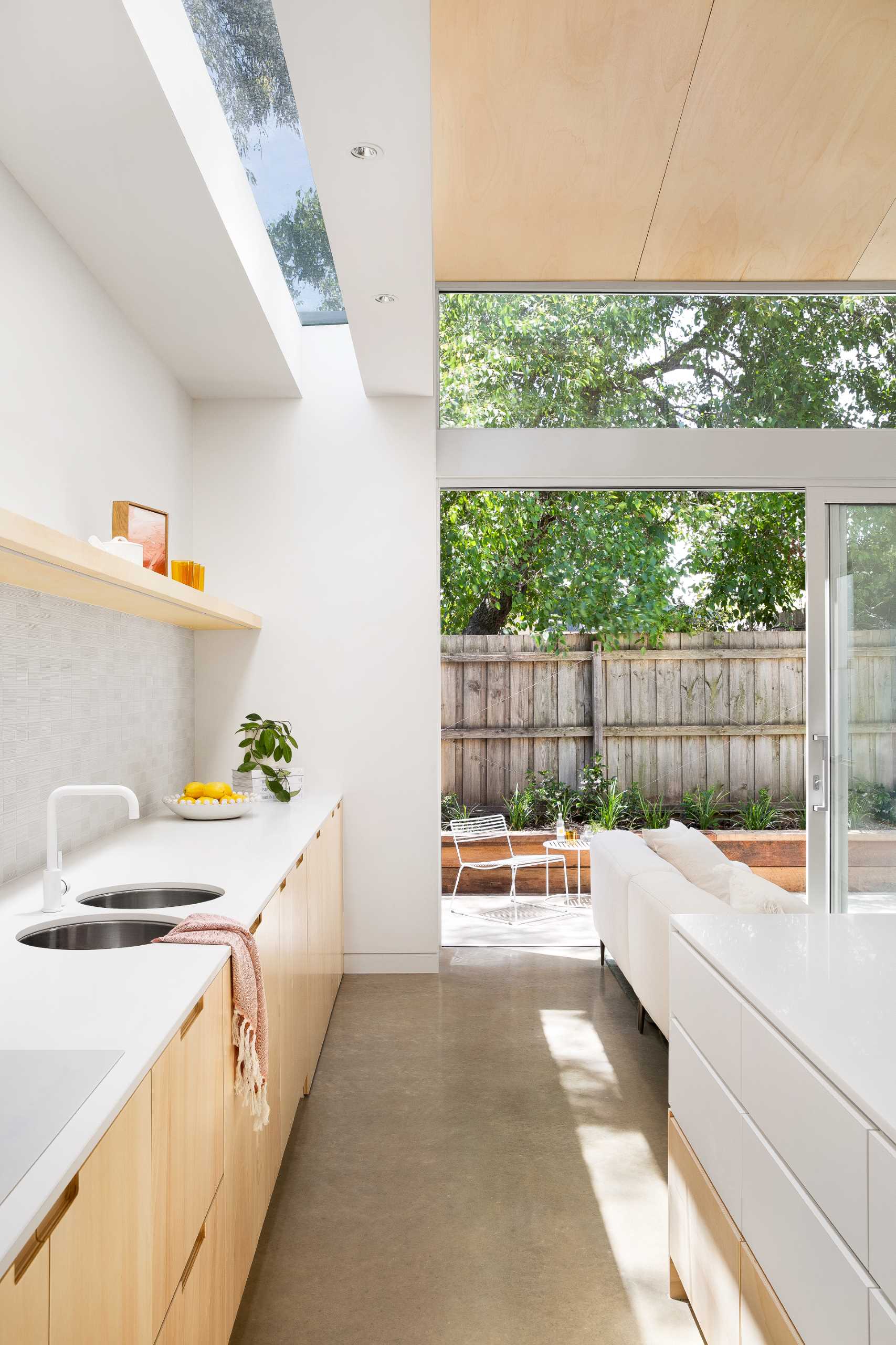 The kitchen, which enjoys natural light from a skylight above and has wood cabinets as well as a floating shelf, is located along the wall and behind the couch.