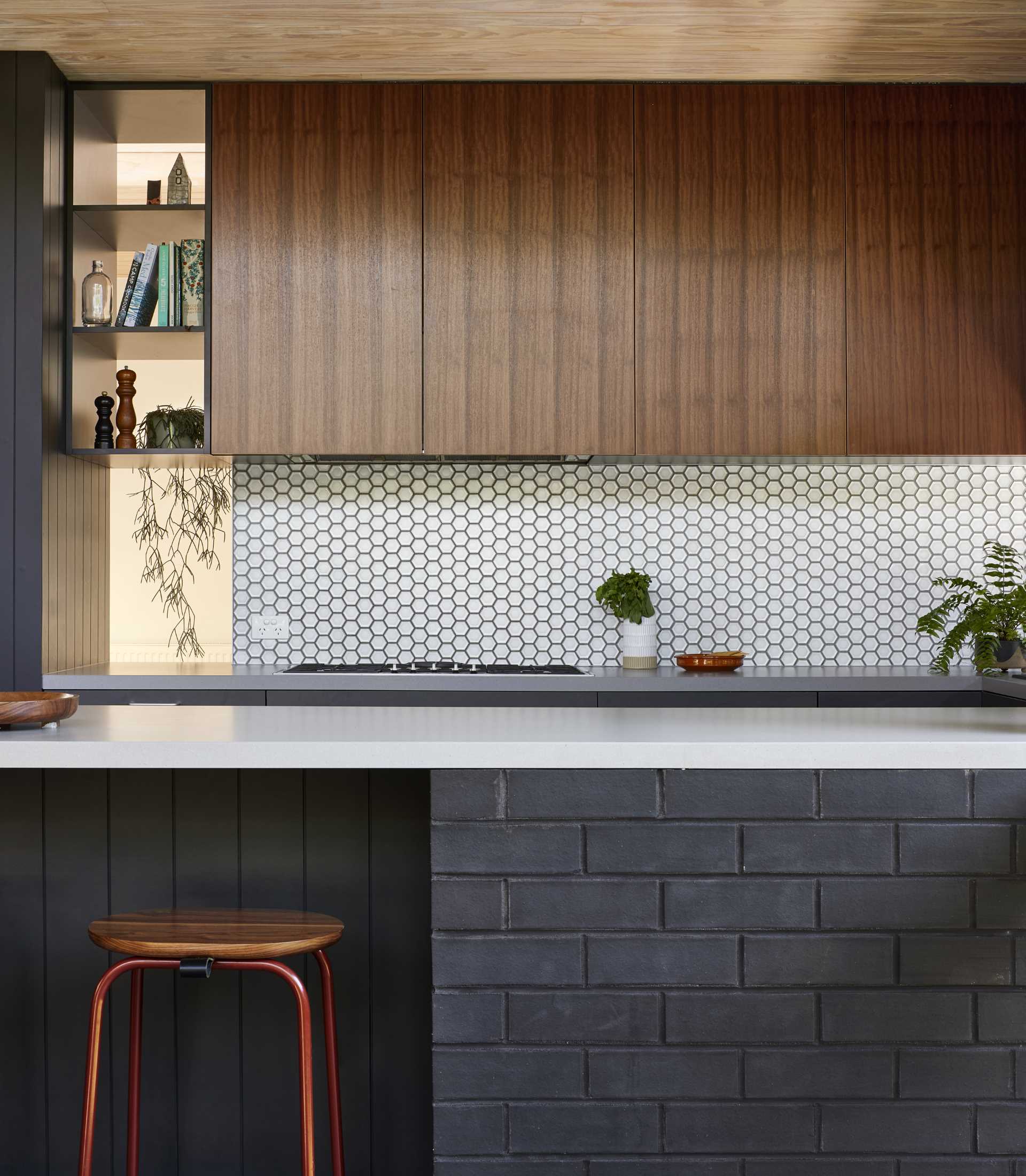 A modern kitchen with wood cabinets, dark grey bricks, and a hexagonal tile backsplash.