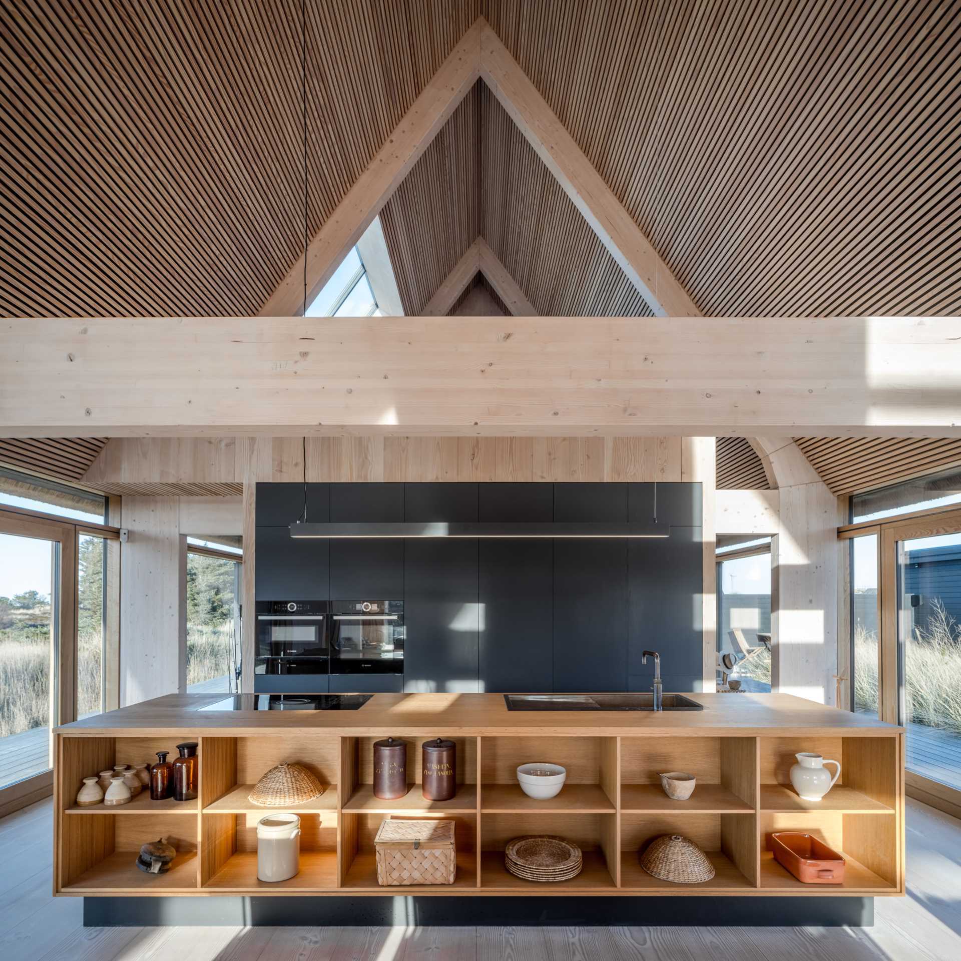 This modern kitchen includes black cabinetry, which complements the exterior of the home, while the large wood island features open shelving.