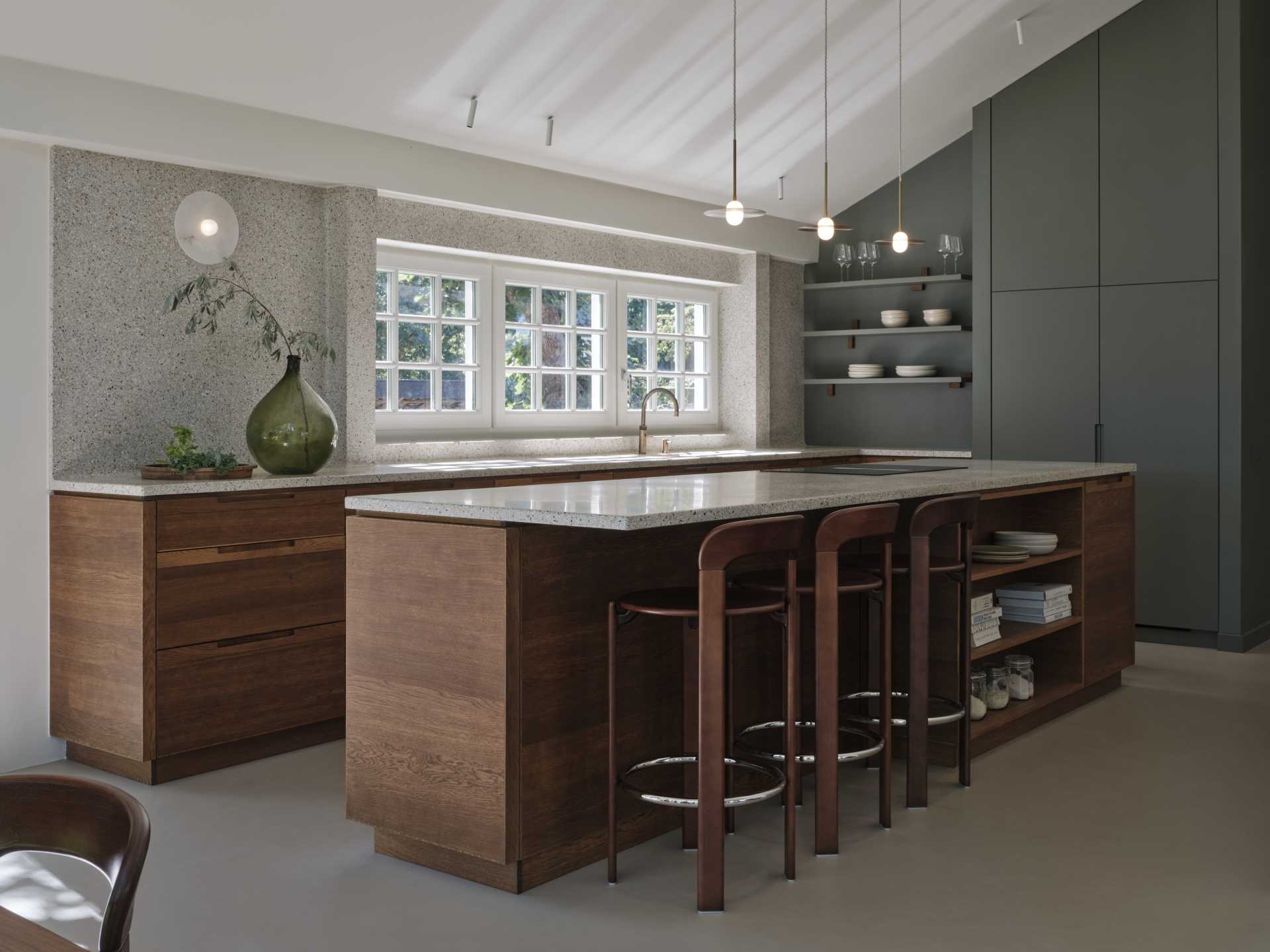 A modern kitchen with dark wood and matte green cabinets, also includes a seamless terrazzo countertop and integrated sink, that then travels up onto the wall.