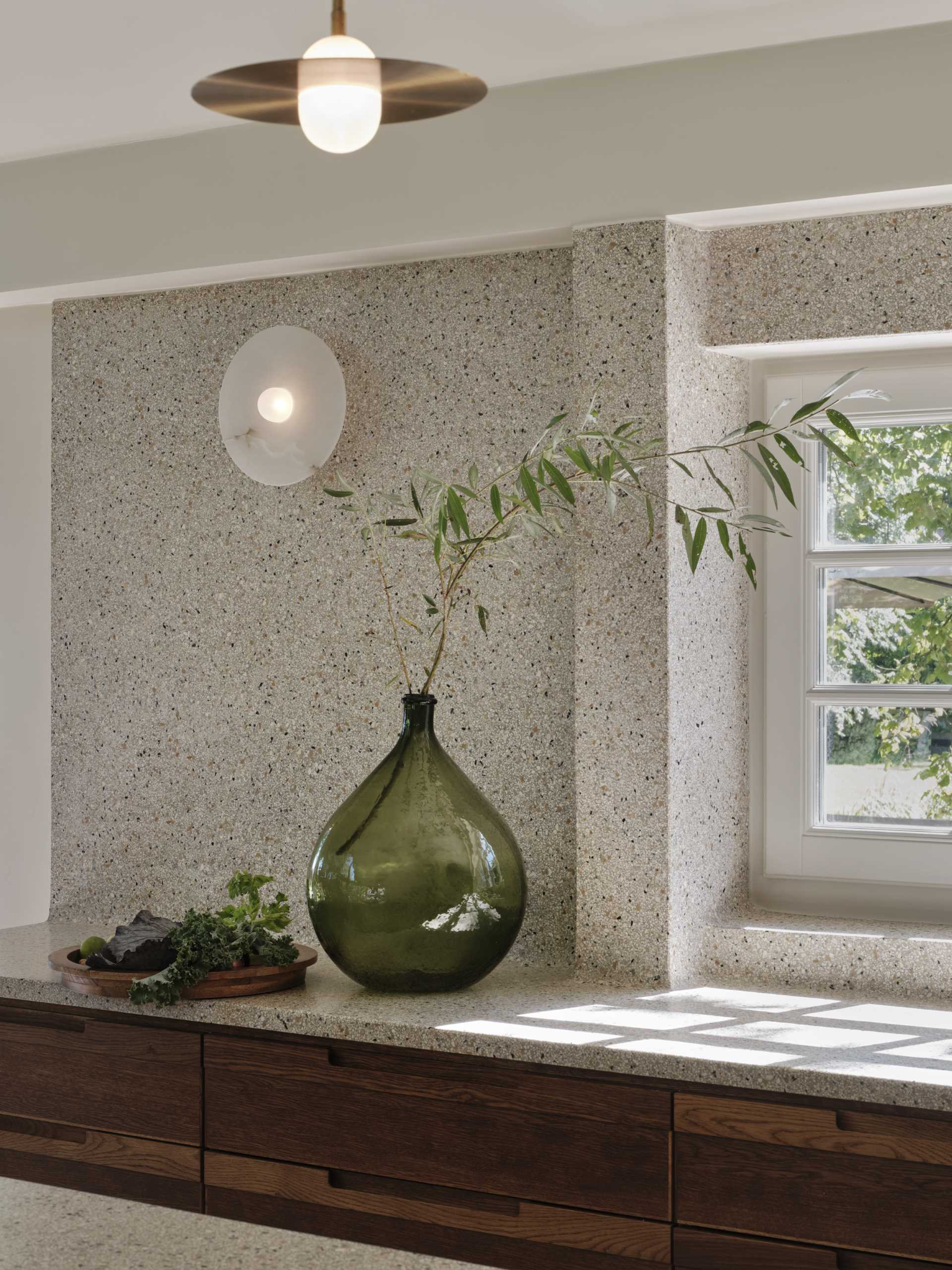 A modern kitchen with dark wood and matte green cabinets, also includes a seamless terrazzo countertop and integrated sink, that then travels up onto the wall.