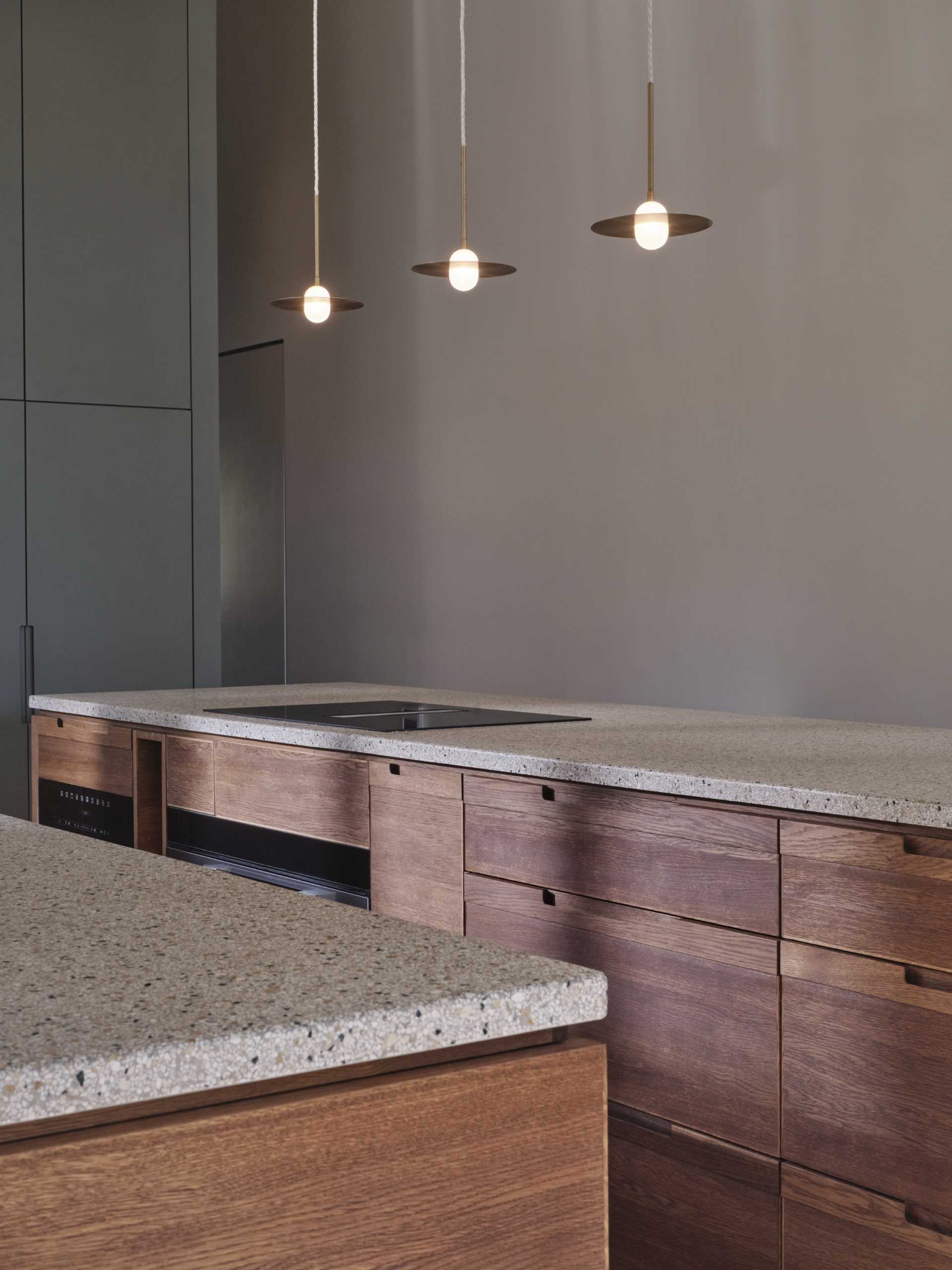 A modern kitchen with dark wood and matte green cabinets, also includes a seamless terrazzo countertop and integrated sink, that then travels up onto the wall.