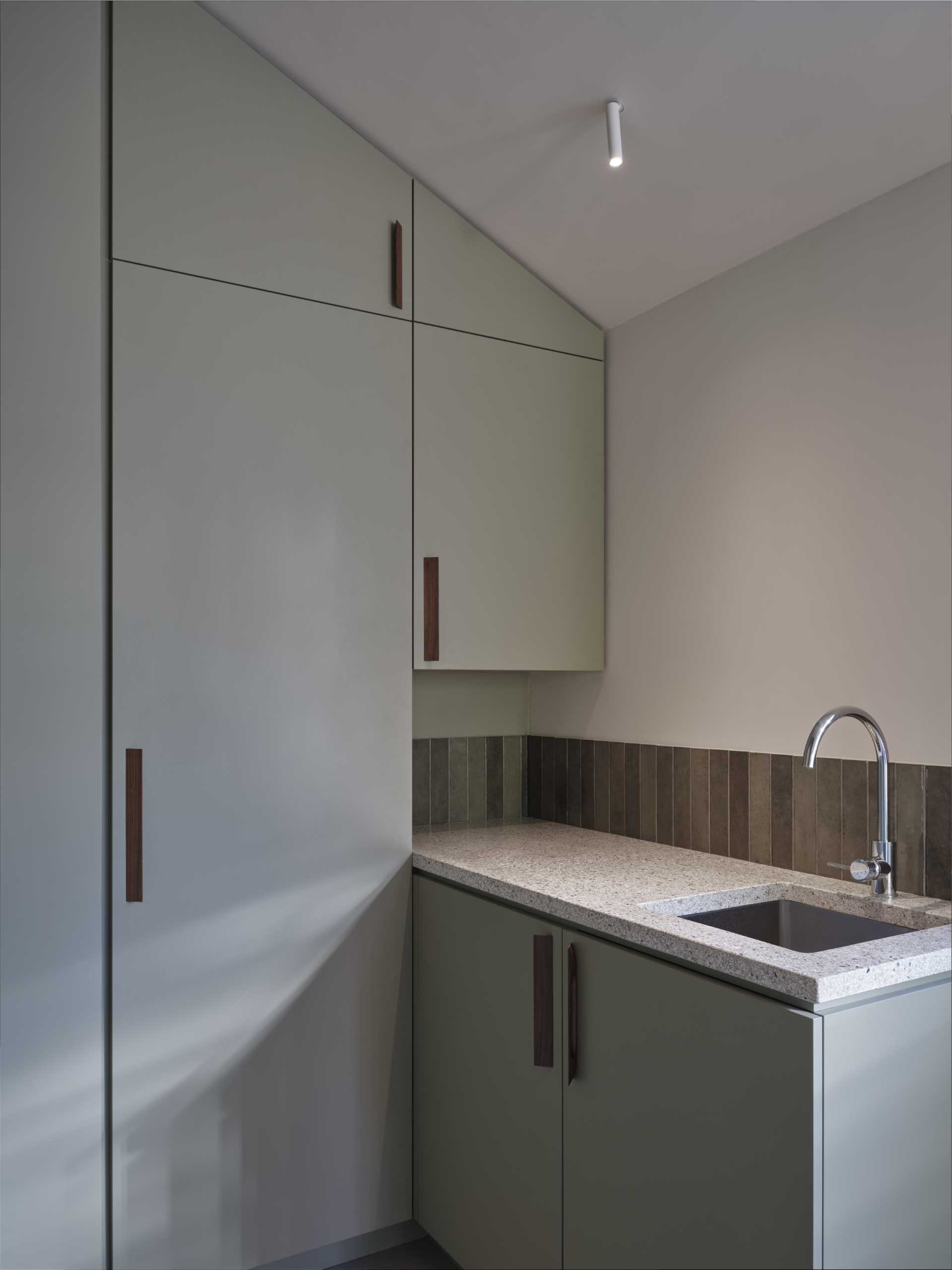 A modern laundry room with terrazzo countertop and sink, and matte green cabinets.