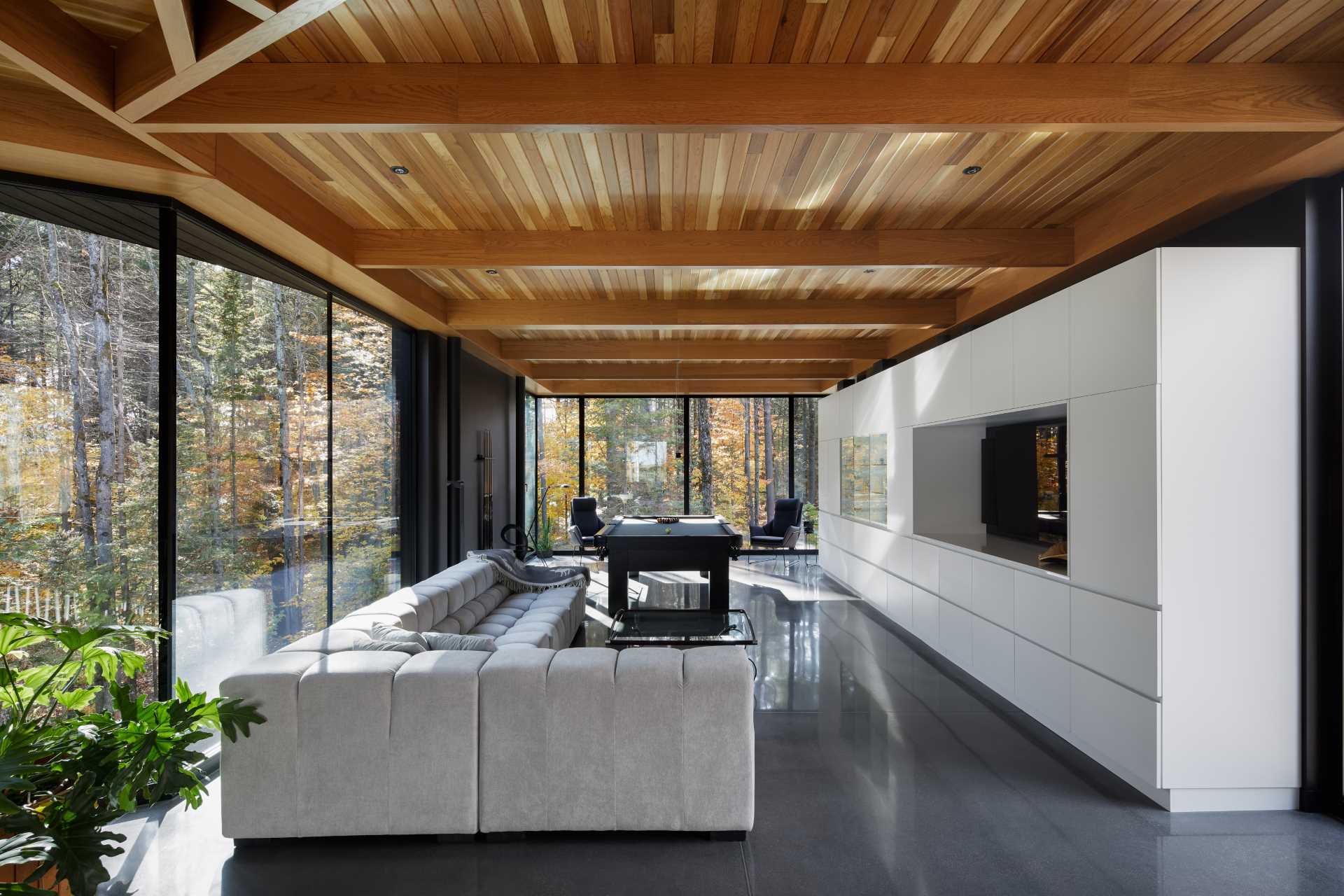 A secondary living room with a large couch and games area is filled with natural light from the floor-to-ceiling windows.