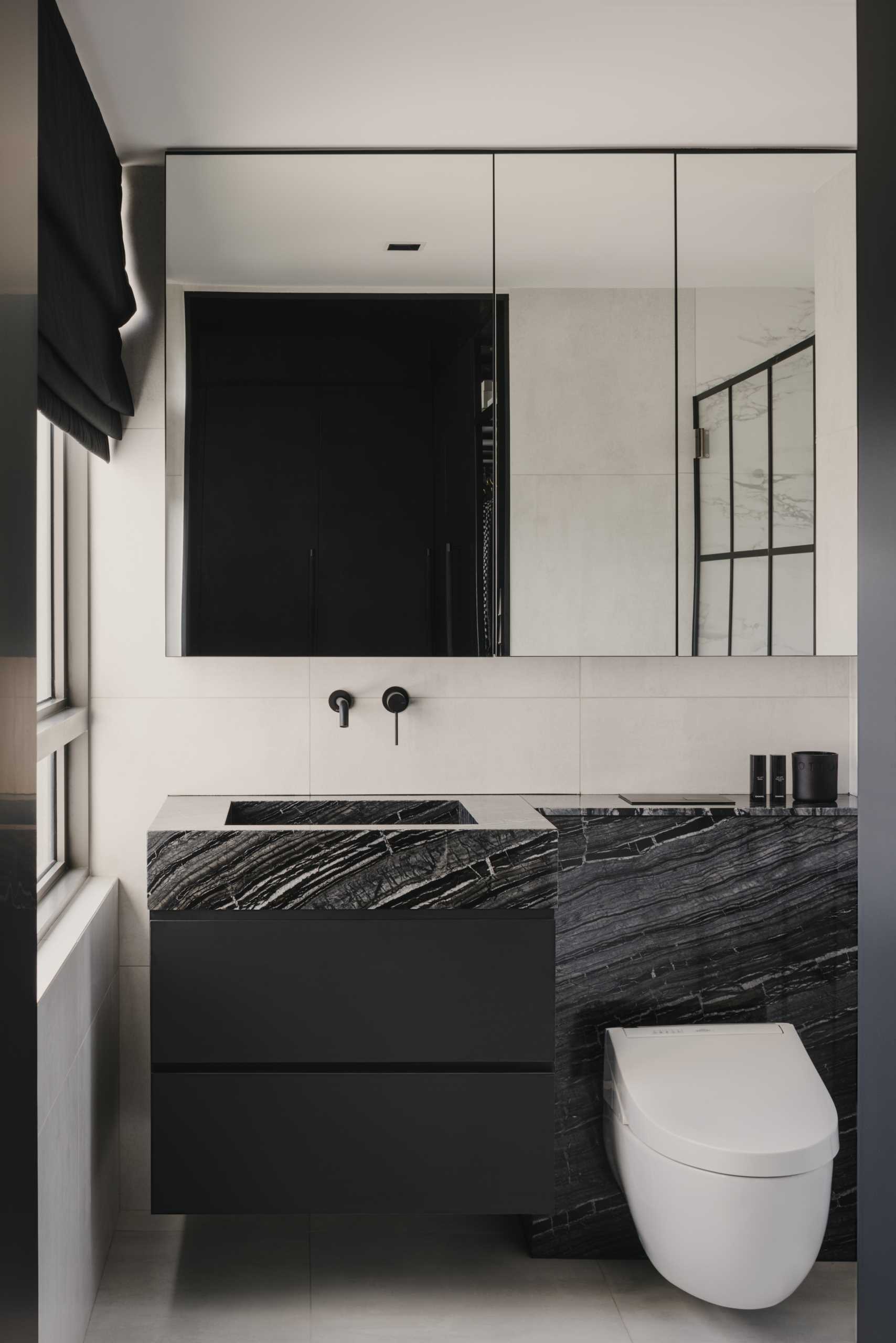 A modern bathroom with a monochrome theme, includes a black vanity, a stone countertop, and a s،wer with black accents.