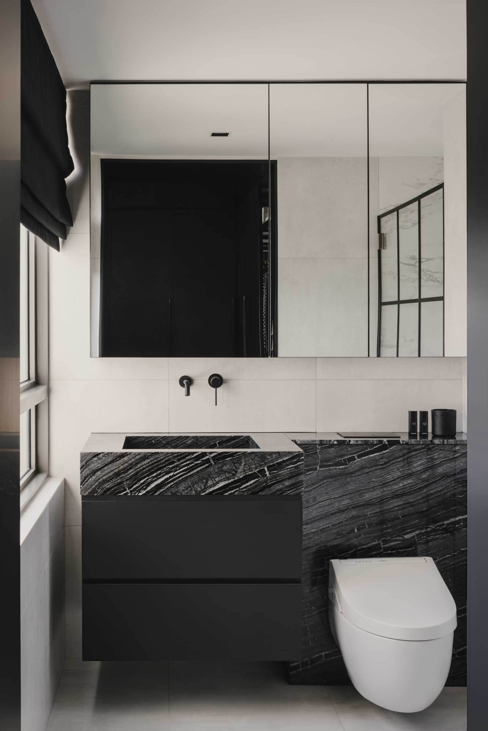 A modern bathroom with a monochrome theme, includes a black vanity, a stone countertop, and a shower with black accents.