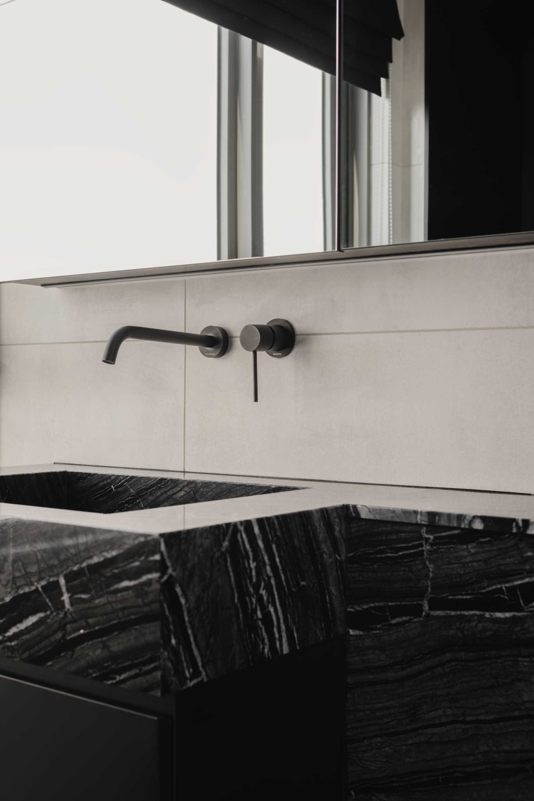 A modern bathroom with a monochrome theme, includes a black vanity, a stone countertop, and a shower with black accents.