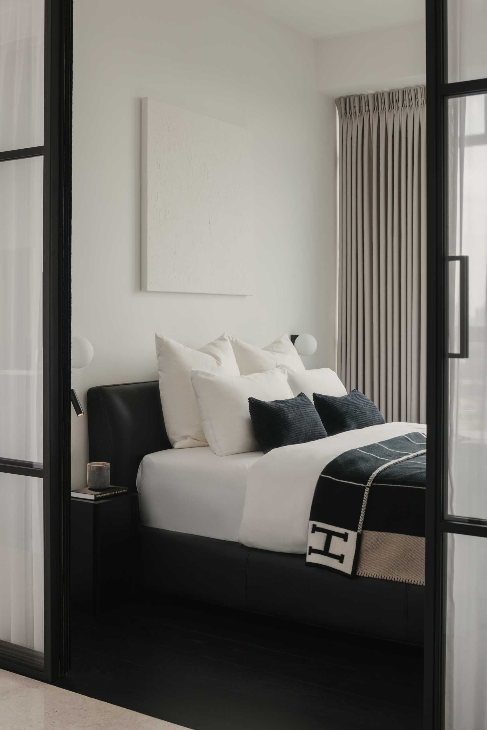A monochromatic bedroom with black flooring allows the bed frame and bedside table to blend in, while the white artwork almost disappears into its surroundings.