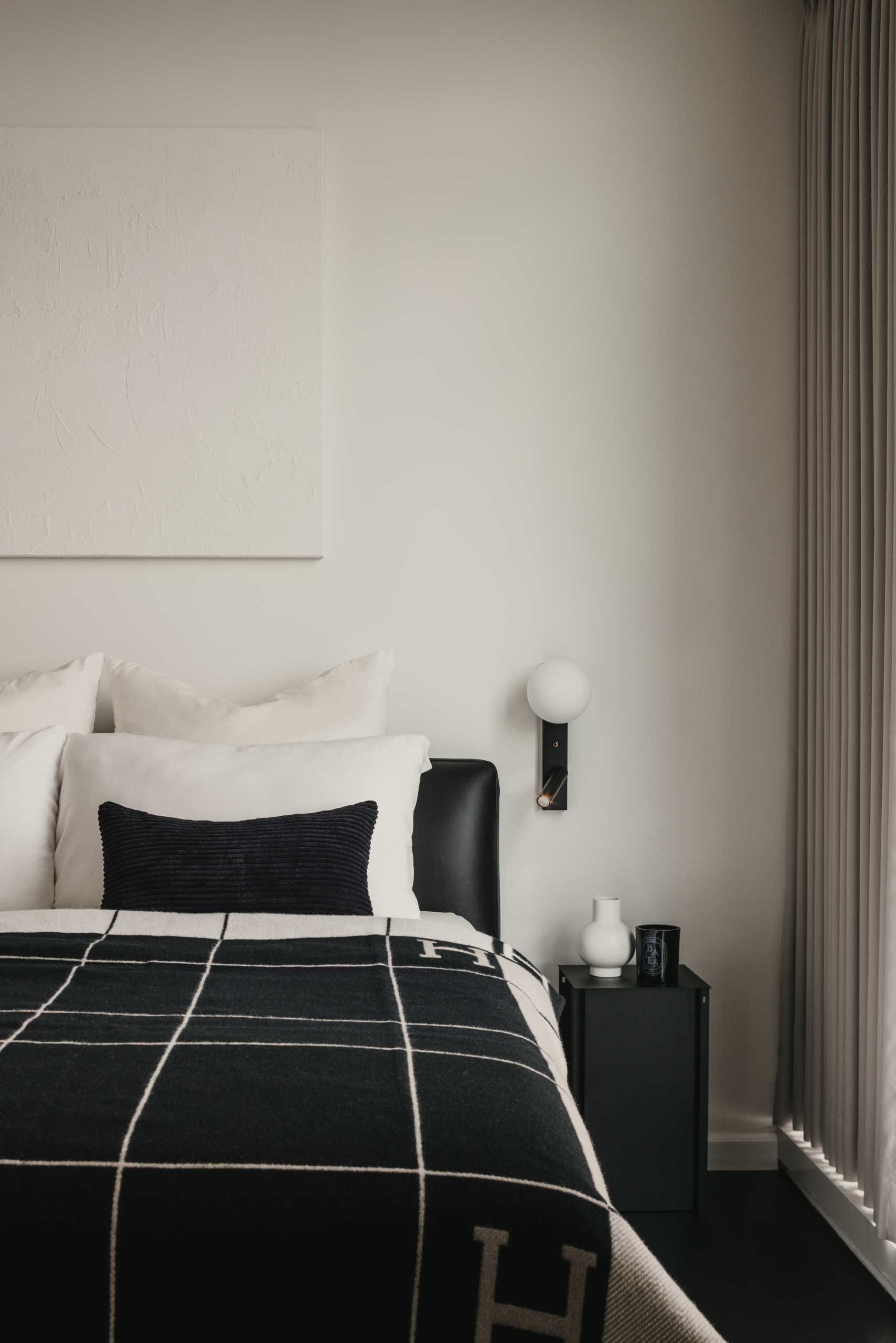 A monochromatic bedroom with black flooring allows the bed frame and bedside table to blend in, while the white artwork almost disappears into its surroundings.