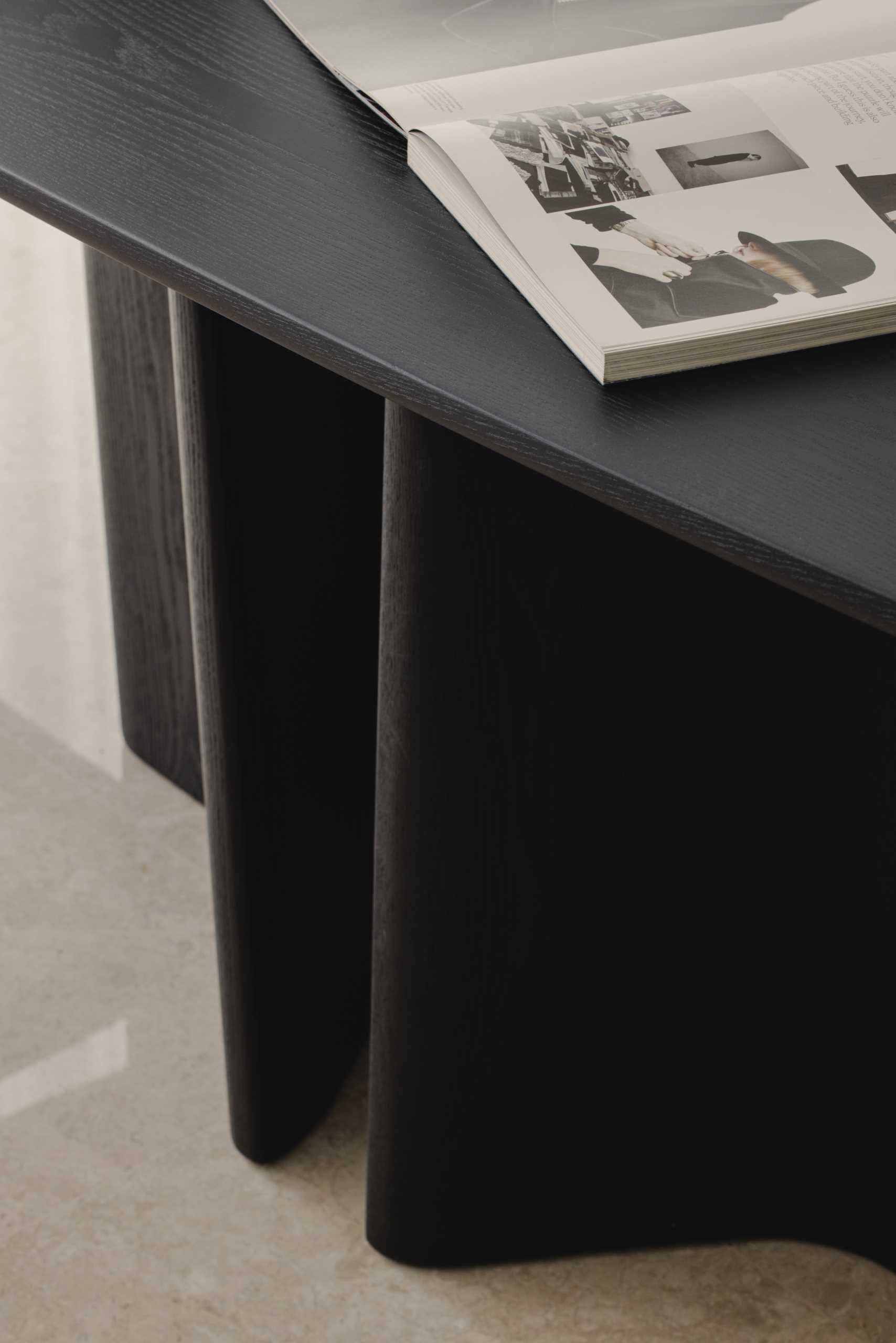 This modern and monochrome dining area is located behind the living room and includes a black dining table with a sculptural base, black and grey dining chairs, a black bench, black and white artwork, and wall lights with a brushed gold accent.