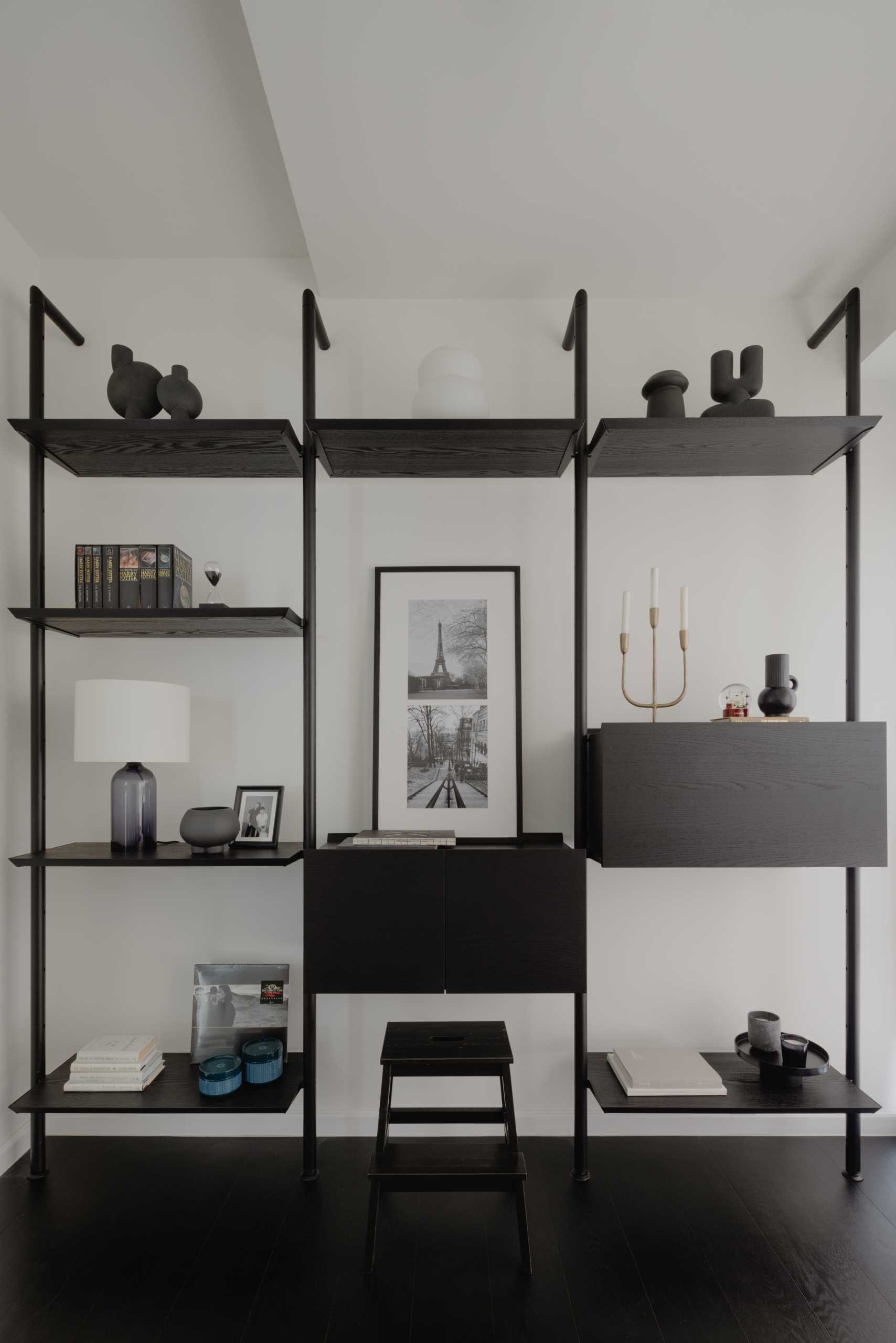 In this monochrome home office, there's a desk by the window, while a shelving unit along the wall showcases additional decorative items and also provides some cabinetry for hidden storage.