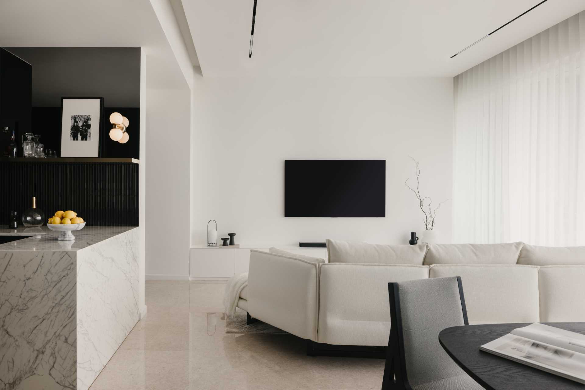 This monochrome living room strikes a balance of light and dark, where a white couch with a mat،g throw blanket is paired with a black coffee table and TV.