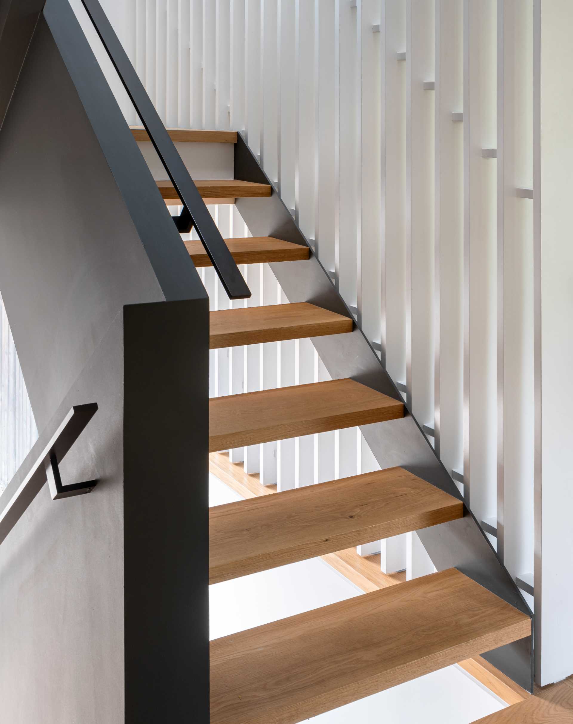 Modern black and wood stairs with a white partition wall.