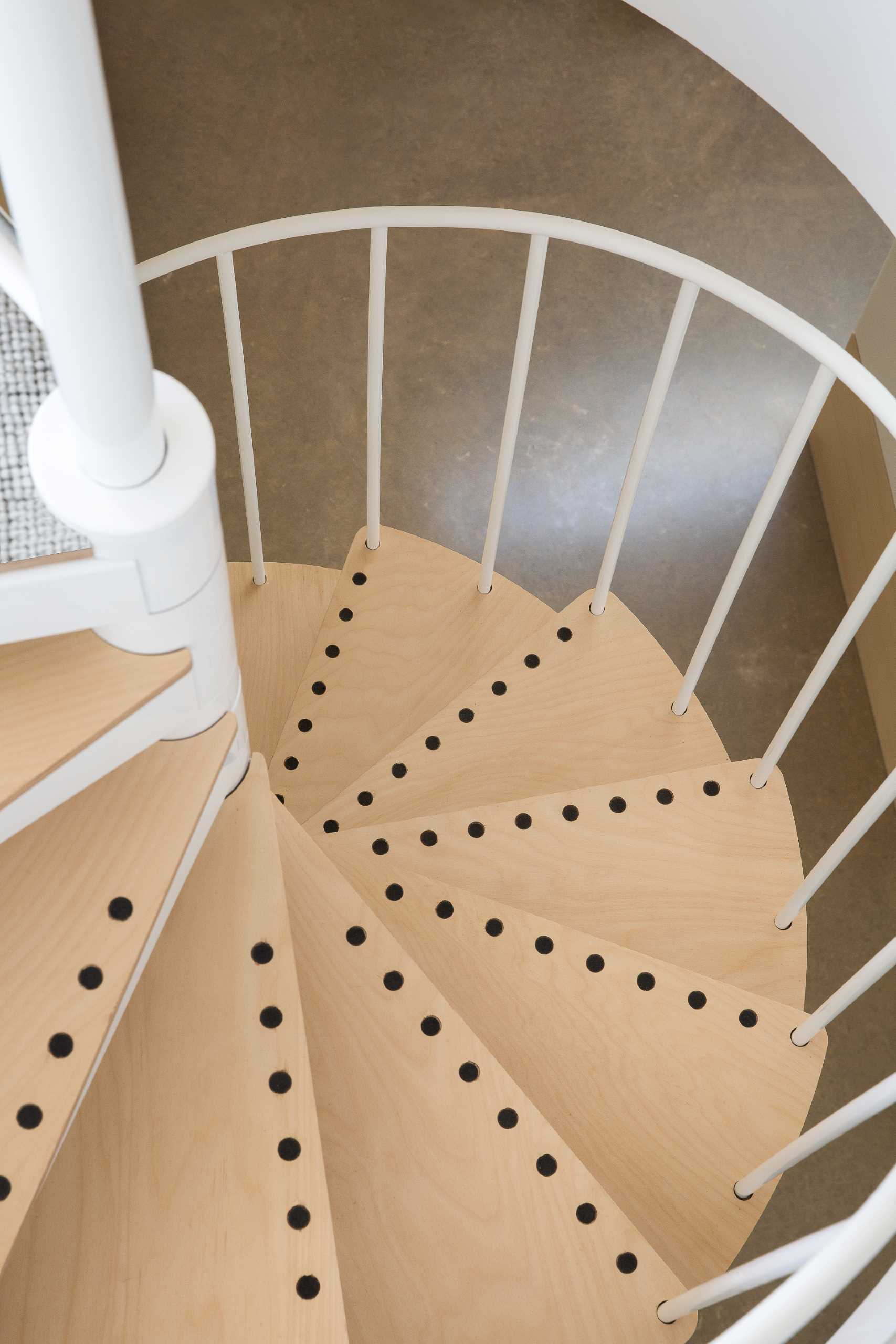 Spiral stairs with a white railing and wood treads lead from the main floor of the home to the upstairs mezzanine level.