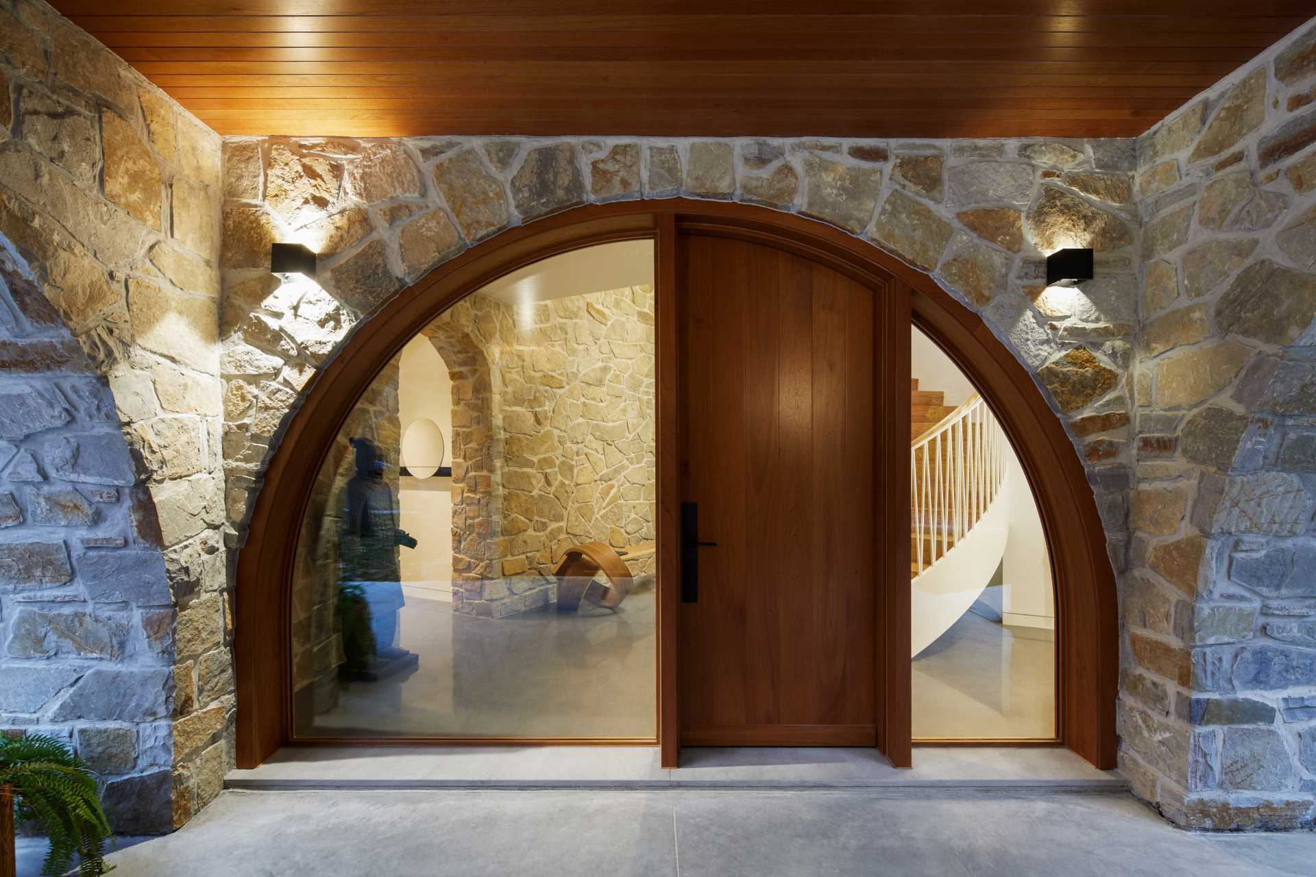 The stone, wood, and glass entrance is accessed through a covered outdoor space, sheltered from the elements, and arched on all four sides. 