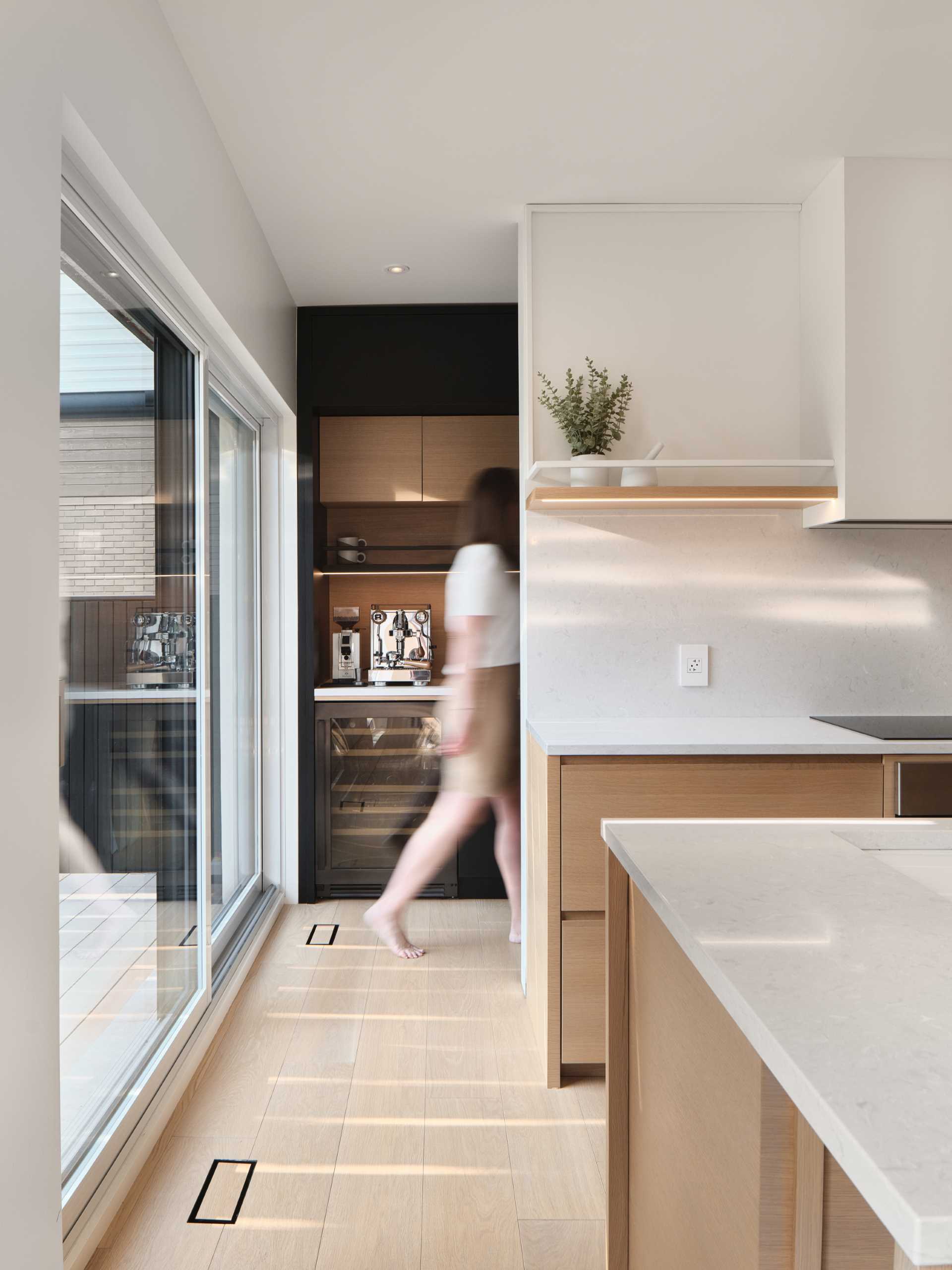 Behind the kitchen is a partially hidden pantry, which has black and wood cabinets, additional counter space, a wine fridge, and an oven.