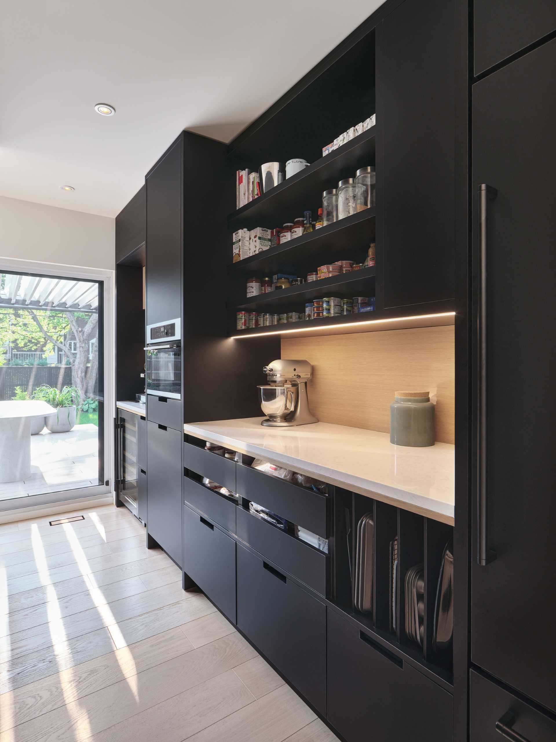 Behind the kitchen is a partially hidden pantry, which has black and wood cabinets, additional counter space, a wine fridge, and an oven.