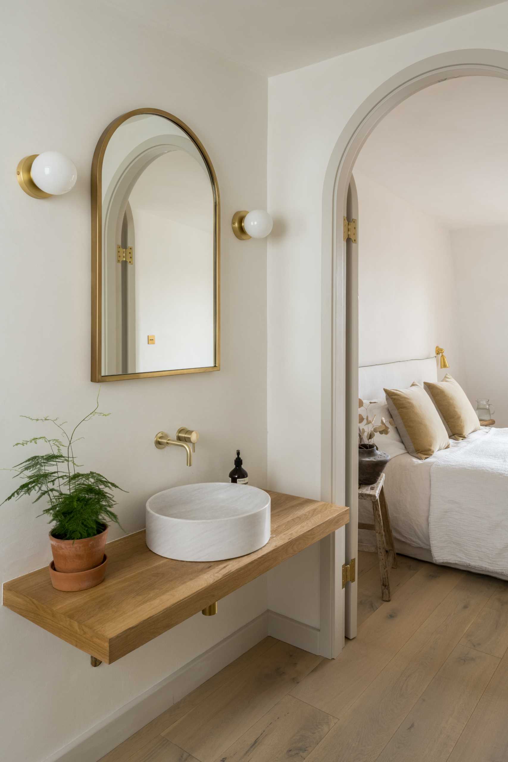 An arched doorway leads from the bedroom to the ensuite bathroom, where there's a freestanding bathtub under the window, a wood vanity, and a shower with a built-in seat.