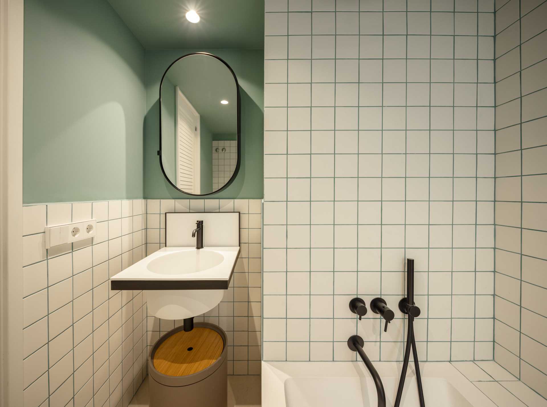 A modern bathroom includes square tiles with green grout that matches the walls, a small vanity, and a built-in bathtub.