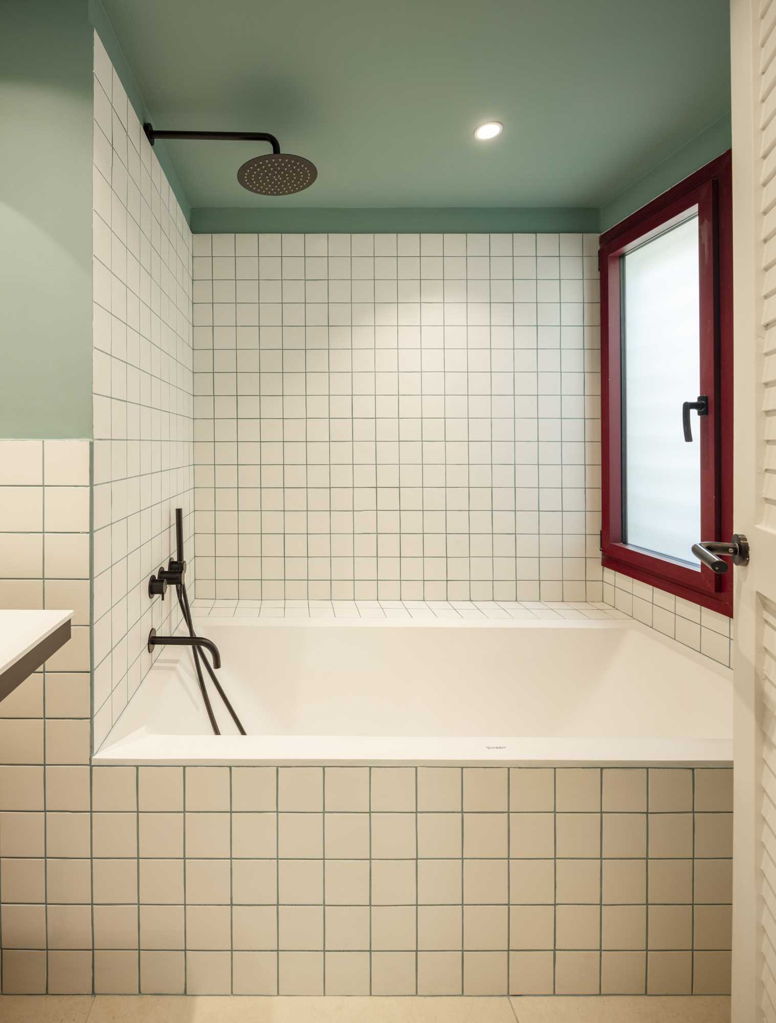 A modern bathroom includes square tiles with green grout that matches the walls, a small vanity, and a built-in bathtub.