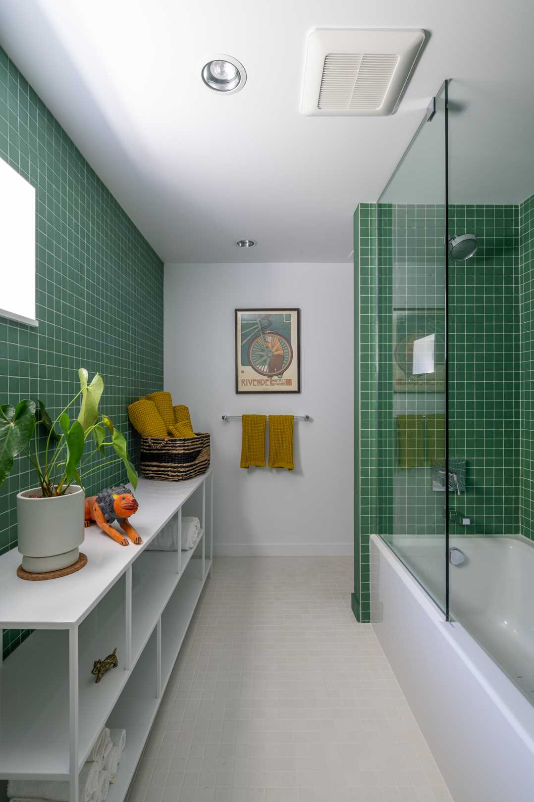 A white and emerald green guest bath, that features small green tiles and a white open shelving unit.
