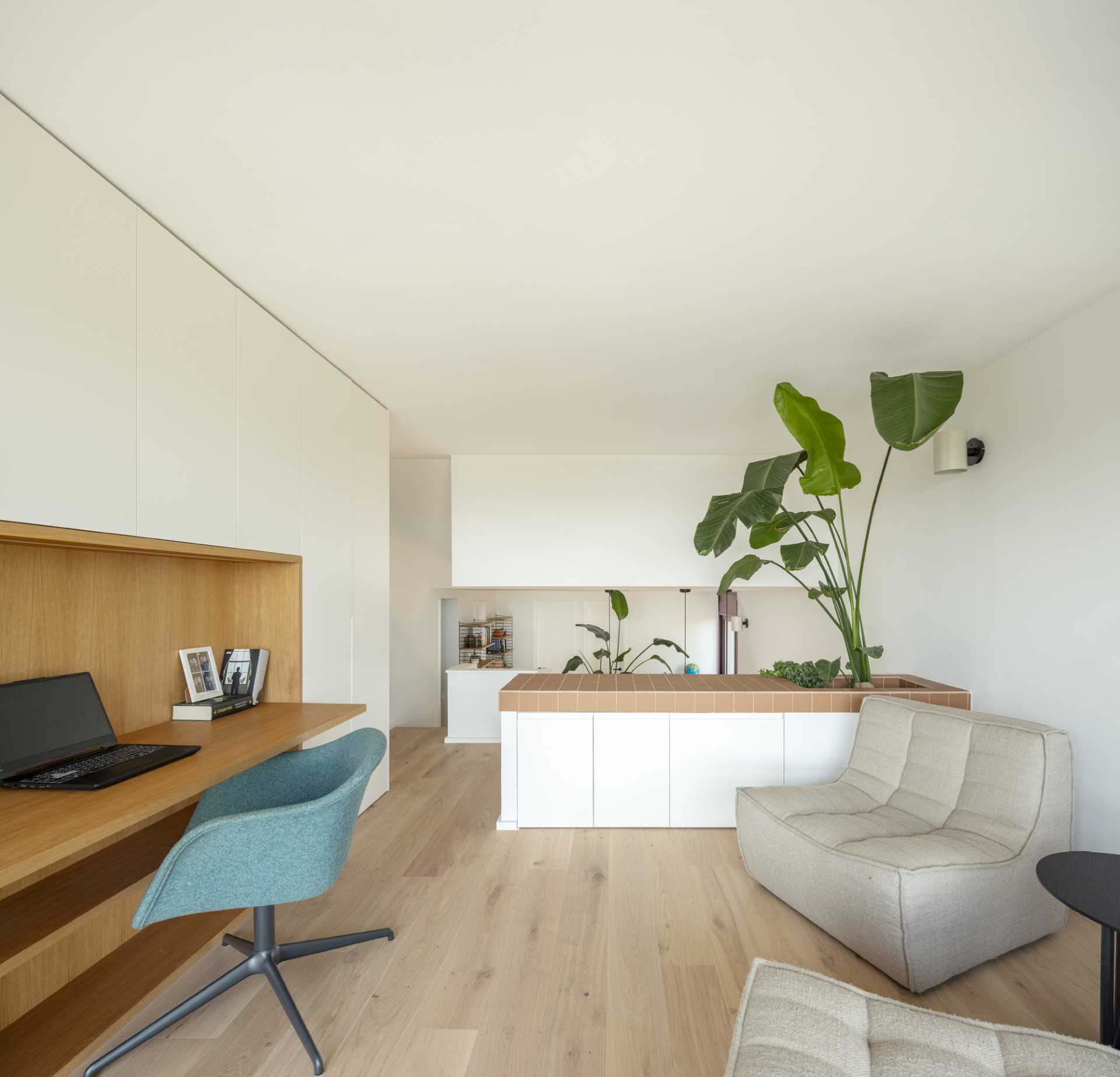 This home office includes cabinetry which is broken up with a wood-lined desk, as well as a seating area and a built-in planter.